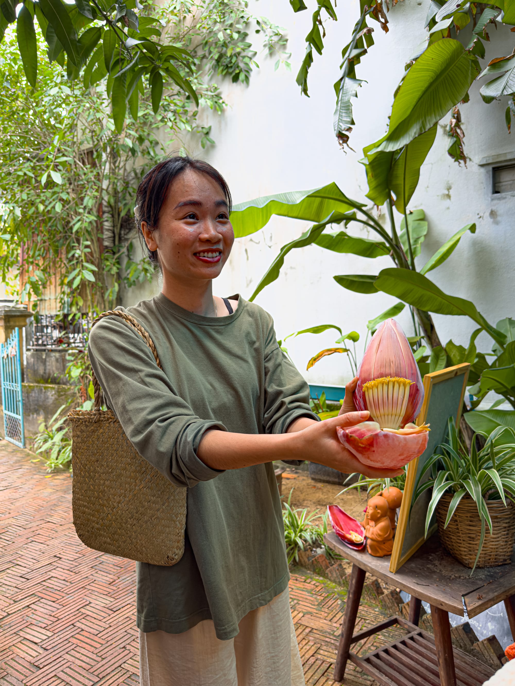 Instructor at Chickpea Eatery vegan cooking class in Hội An holding a freshly cut banana blossom in the courtyard garden, explaining how it will be used in a salad