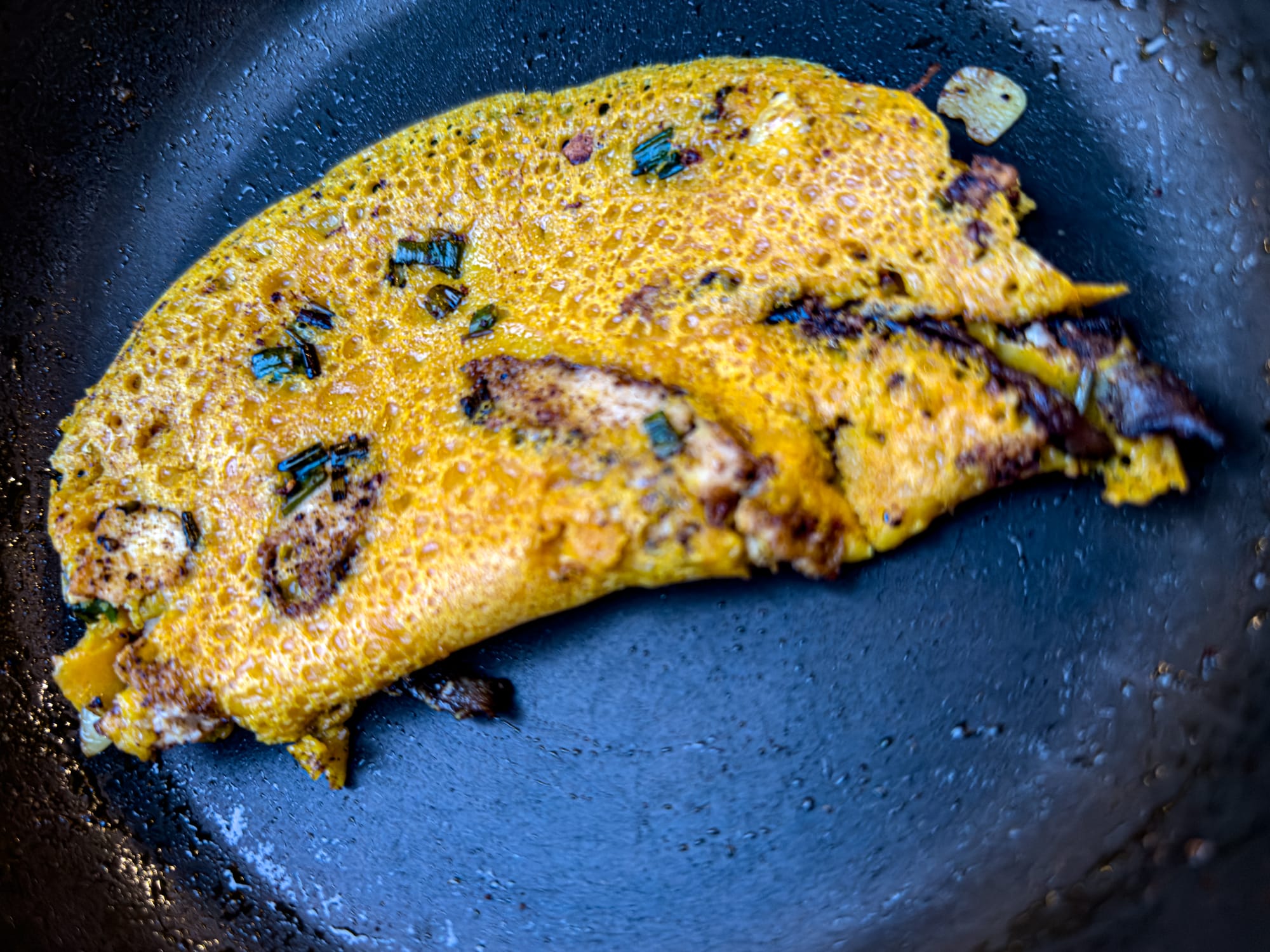 Crispy golden bánh xèo pancake cooking in a skillet at Chickpea Eatery vegan cooking class in Hội An, filled with mushrooms and herbs