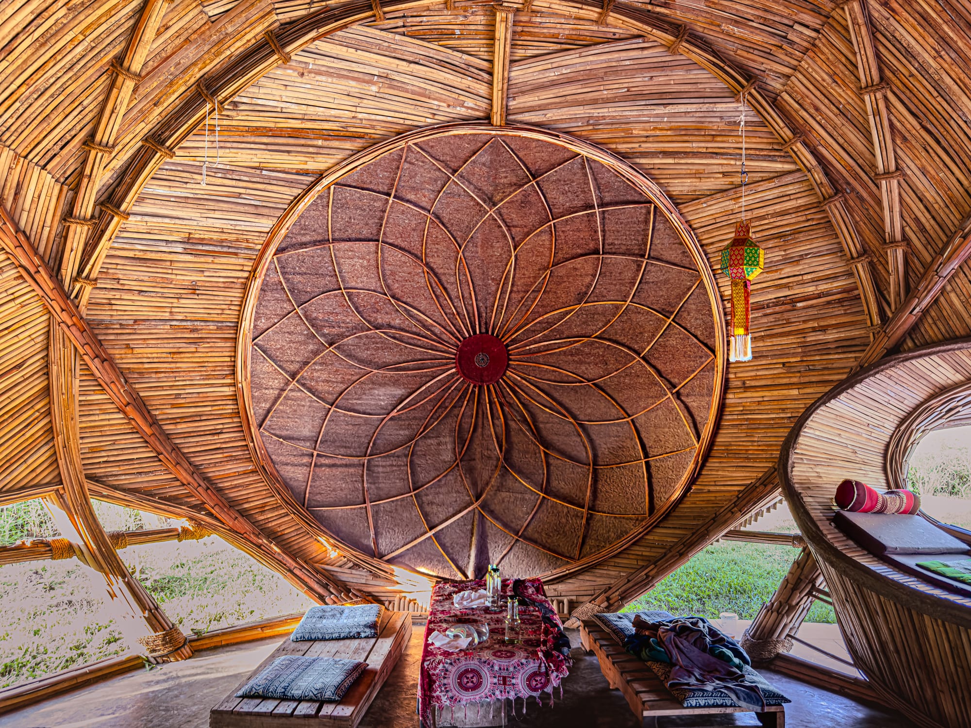 Interior of Cocoon Chiang Mai’s bamboo hall featuring a lotus-shaped sacred geometry ceiling pattern, bamboo walls, and low seating with cushions arranged around a central table