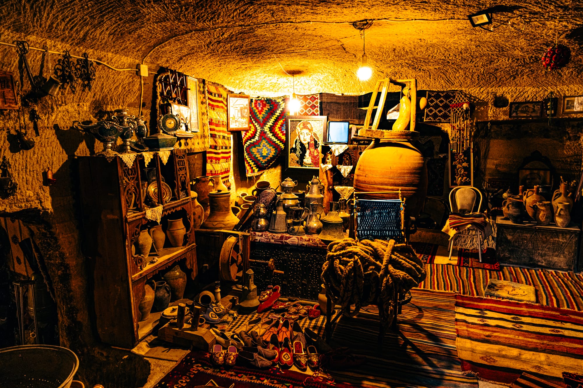 Interior of Cappadocia Cultural Antique Collection cave room filled with pottery, woven rugs, traditional Anatolian artifacts, and vintage household items illuminated by warm lighting