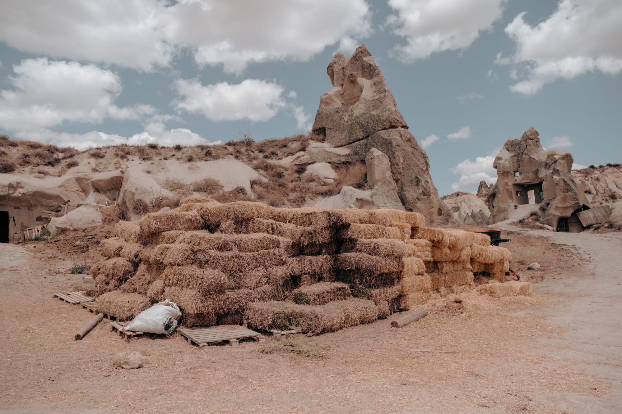 Stack of golden hay bales at Dalton Brothers Ranch in Cappadocia, Turkey, framed by unique fairy chimney rock formations under a partly cloudy sky