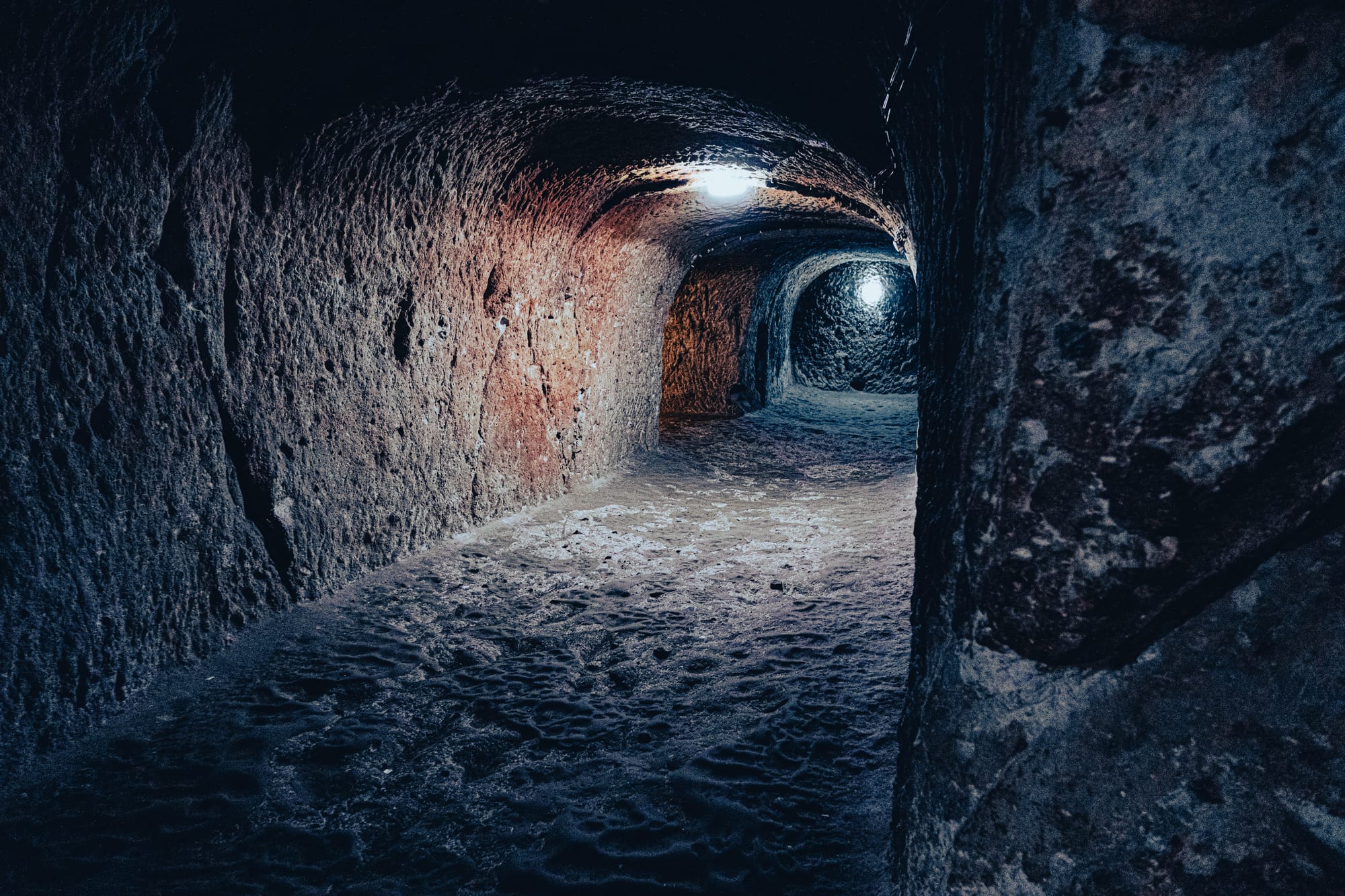 Illuminated tunnel in Derinkuyu Underground City with curved walls and compacted earthen floor in Cappadocia