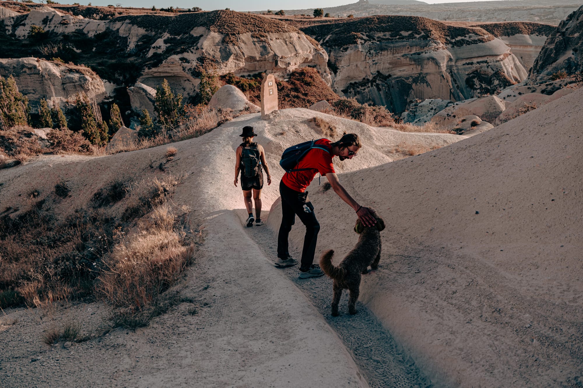 Hikers walk a narrow ridge trail in Cappadocia, Turkey, surrounded by eroded rock formations and soft evening light