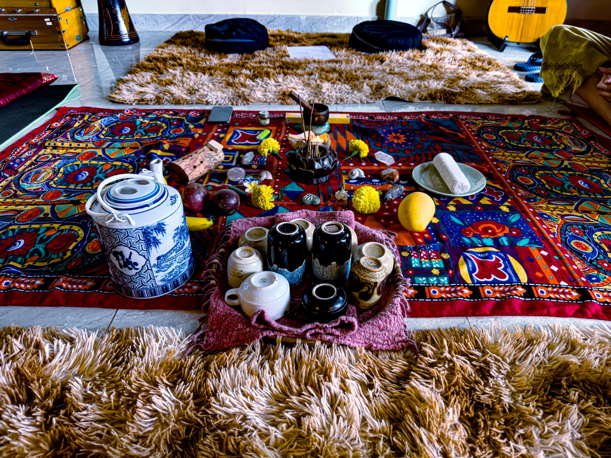 Colorful setup for a women’s circle in Hội An, with patterned cloths, ceramic teapots, cups, fruits, flowers, and incense arranged on a rug surrounded by cushions and mats