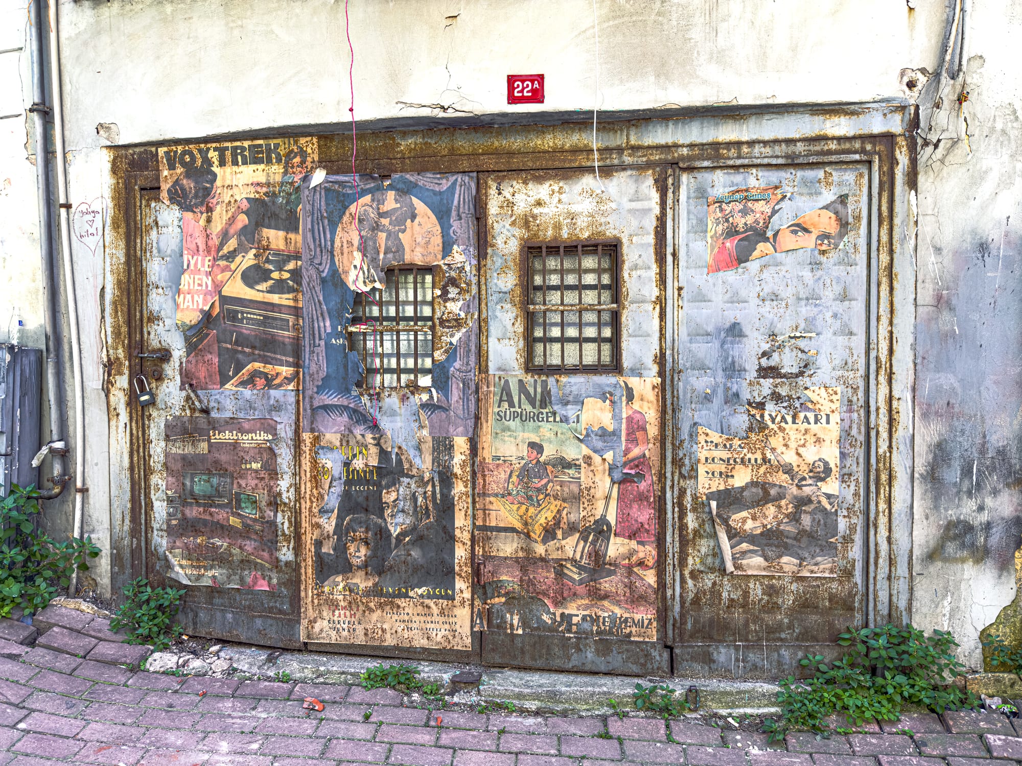 Rusted metal door in Balat plastered with torn vintage posters, showcasing the neighborhood’s gritty, nostalgic charm and texture-rich aesthetic