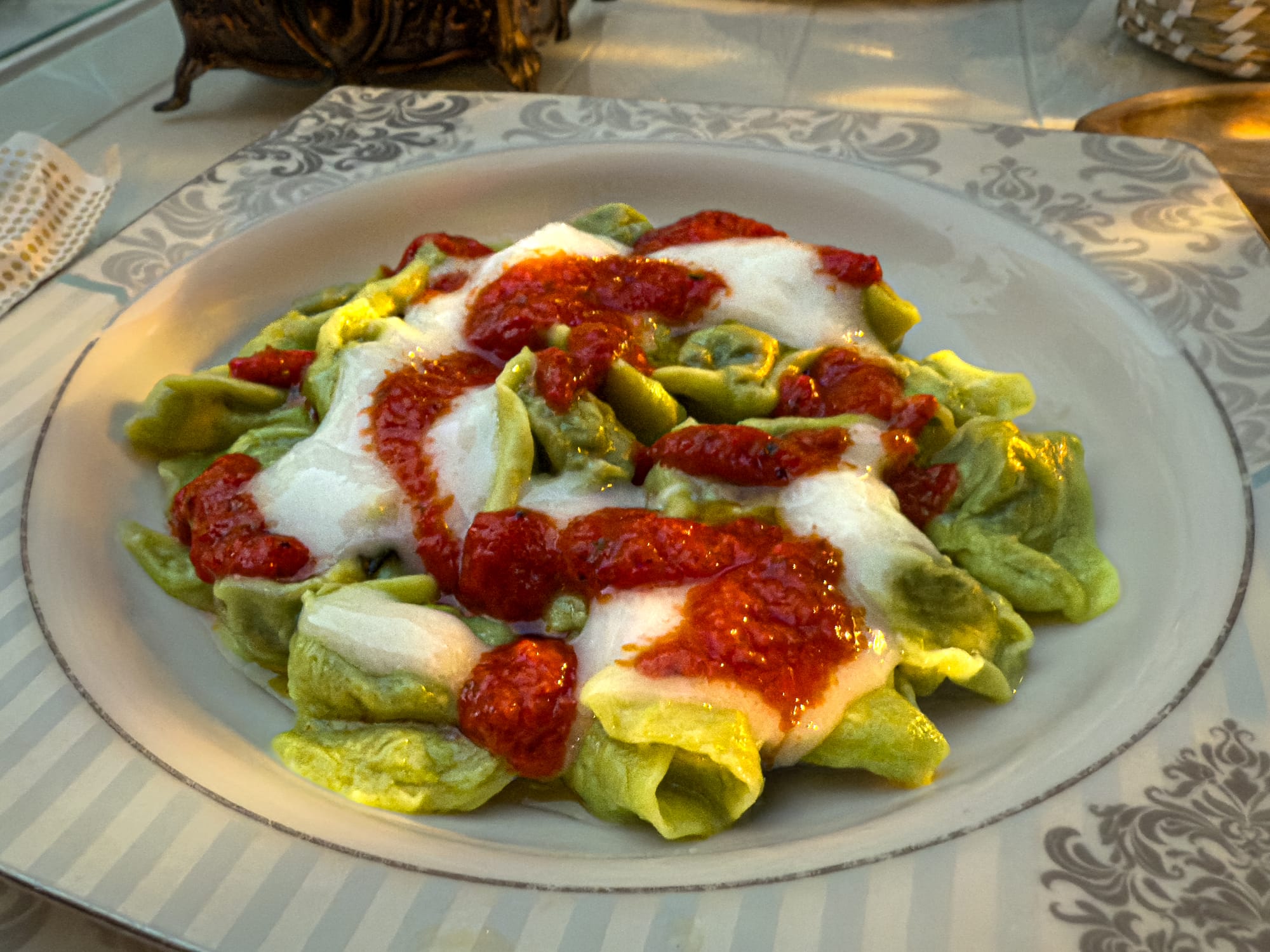 Plate of green vegan manti topped with dairy-free yogurt and red tomato sauce at Fatma Sultan restaurant in Antalya