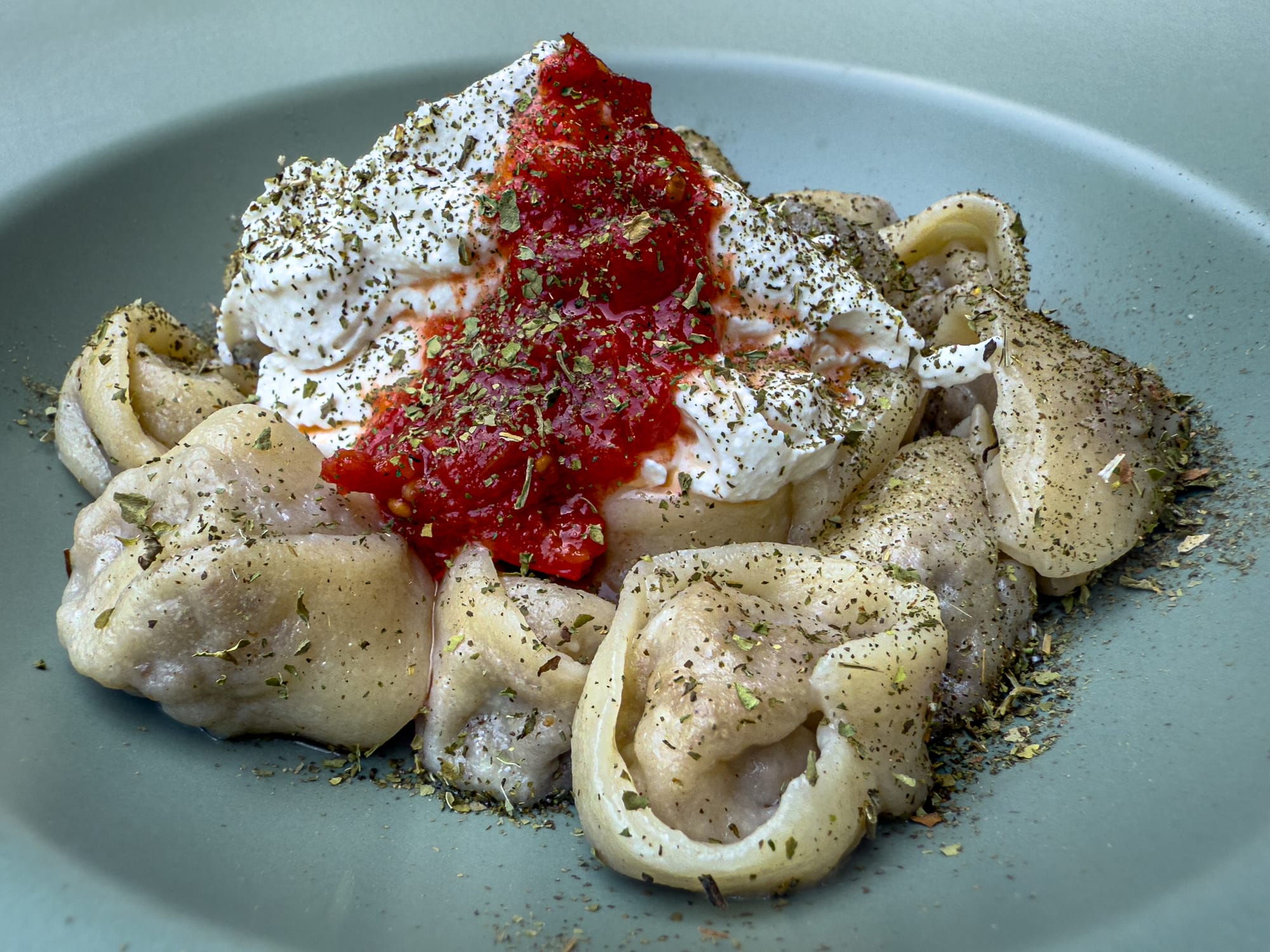Close-up of vegan manti dumplings topped with dairy-free yogurt, tomato sauce, and herbs at Vegan House in Antalya