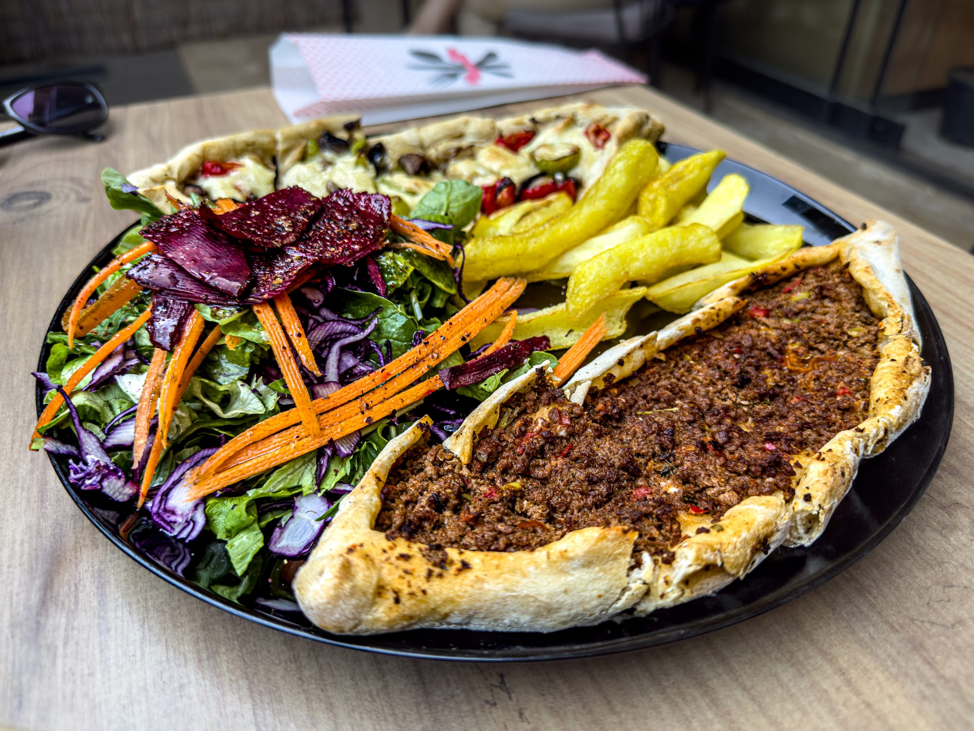 Plate with vegan Turkish pide topped with plant-based meat, served with fries, shredded carrot and beet salad, and roasted vegetables at Vegan House in Antalya