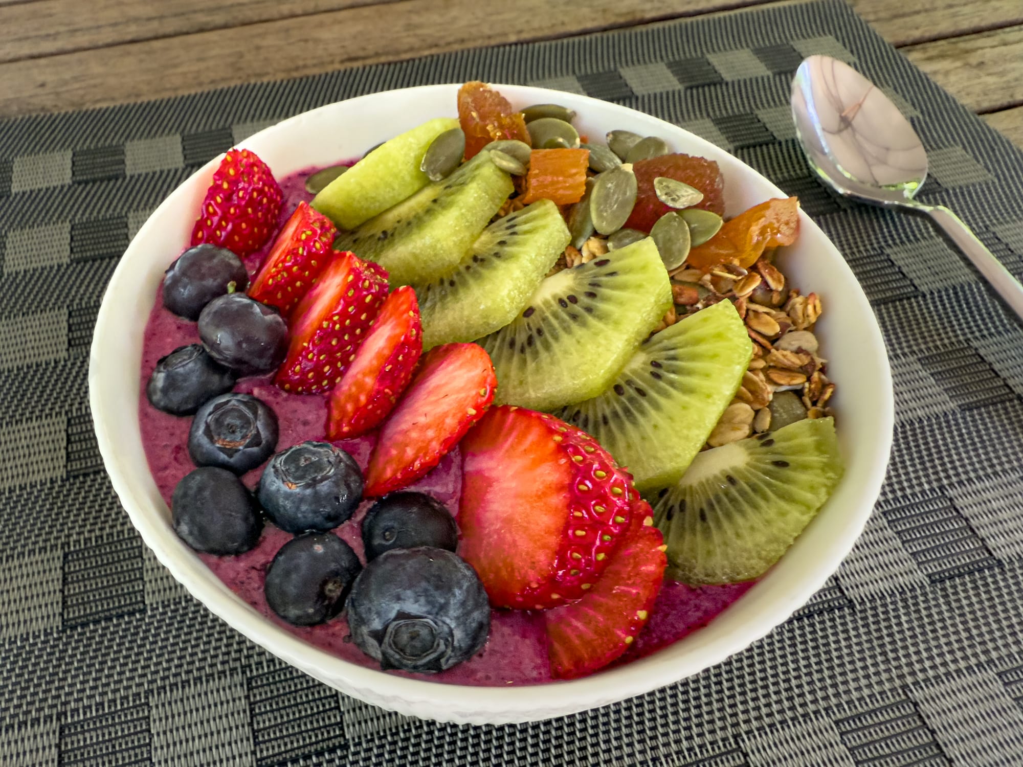 Vibrant acai bowl topped with sliced kiwi, strawberries, blueberries, pumpkin seeds, granola, and dried fruit