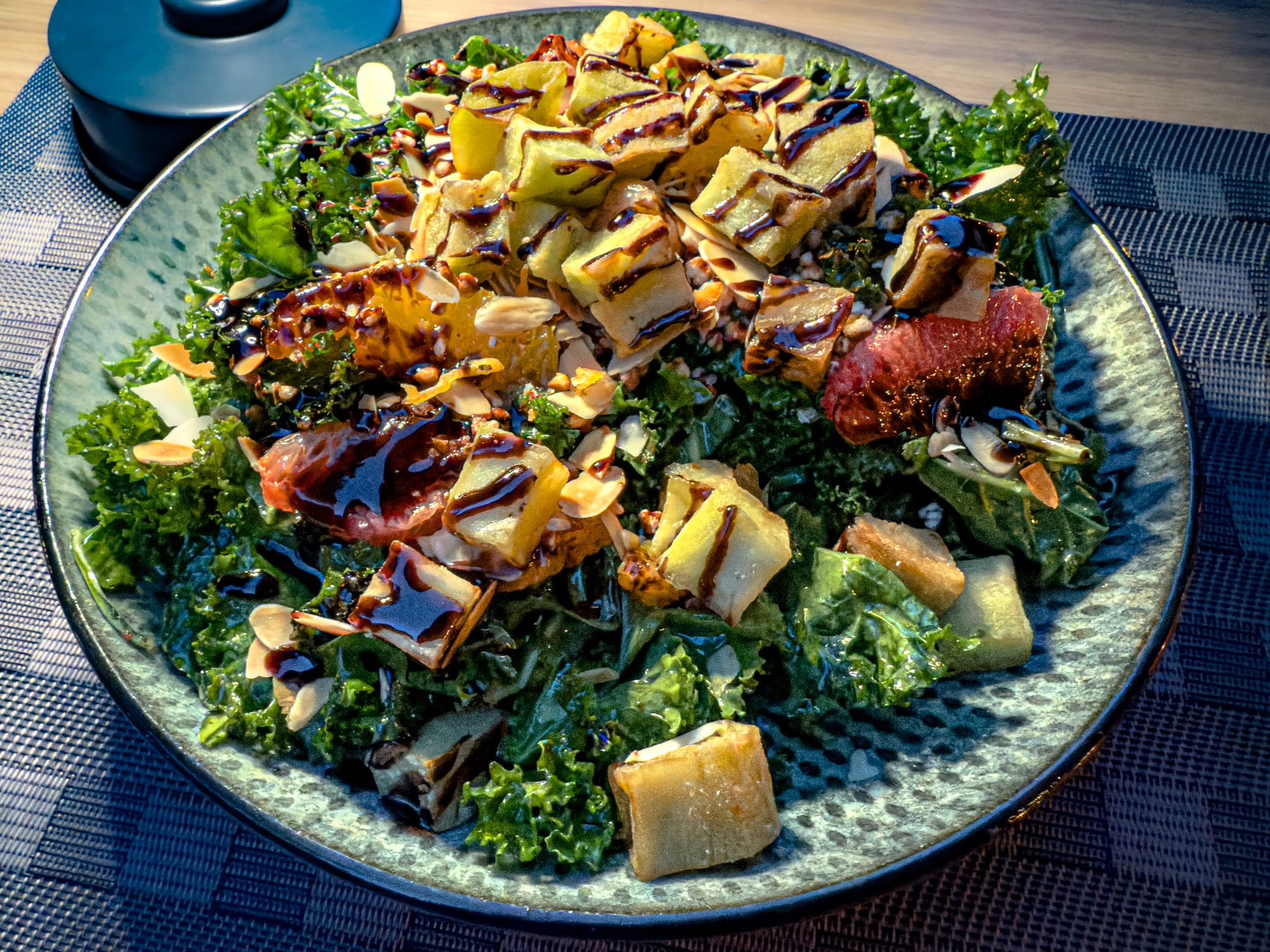 Colorful kale salad with roasted vegetables, citrus slices, toasted almonds, and a dark dressing