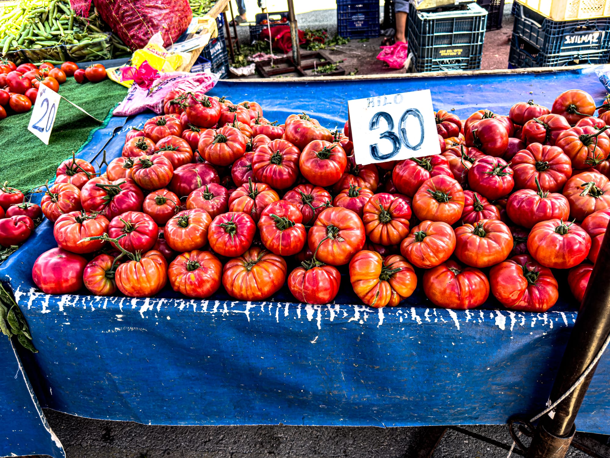 Heirloom-style red tomatoes stacked on a blue tarp with handwritten price sign at Antalya’s Friday Market