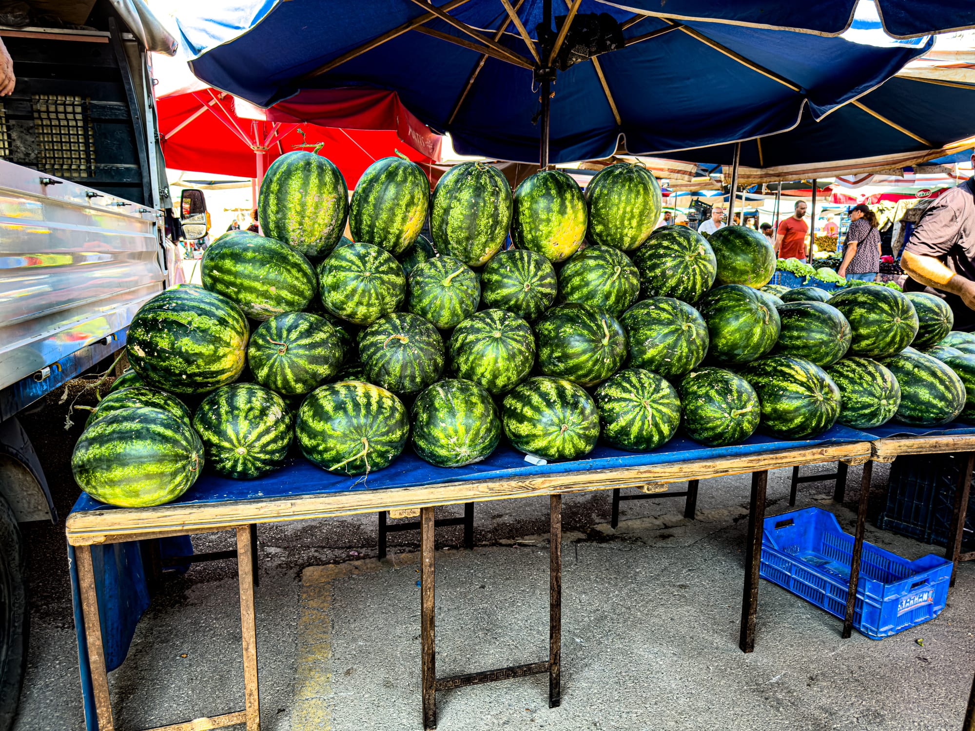 Stacked watermelons on a vendor table under umbrellas at Antalya’s Friday Market
