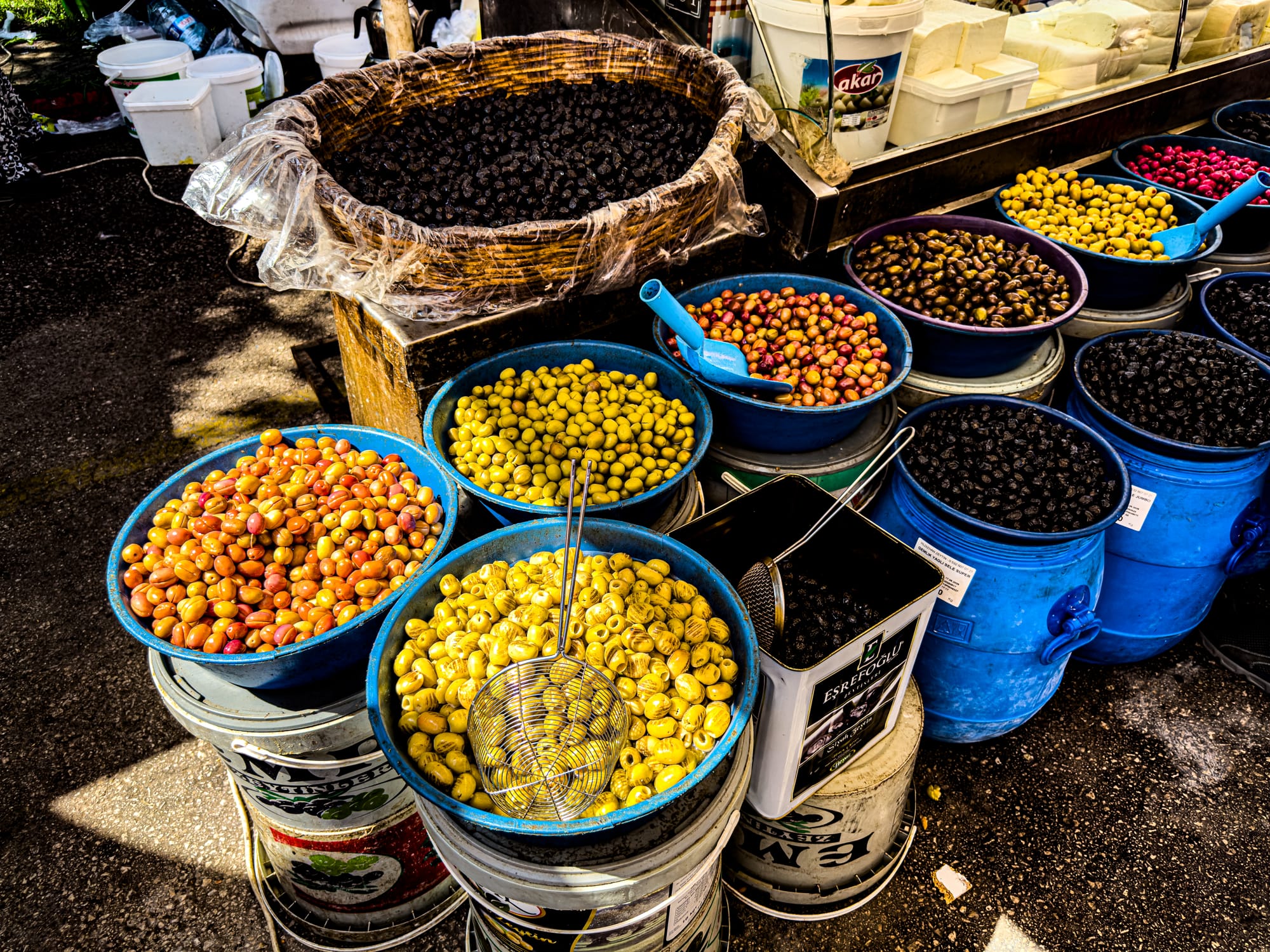 Colorful variety of olives in plastic tubs for sale at Antalya’s Friday Market with scoops and strainers