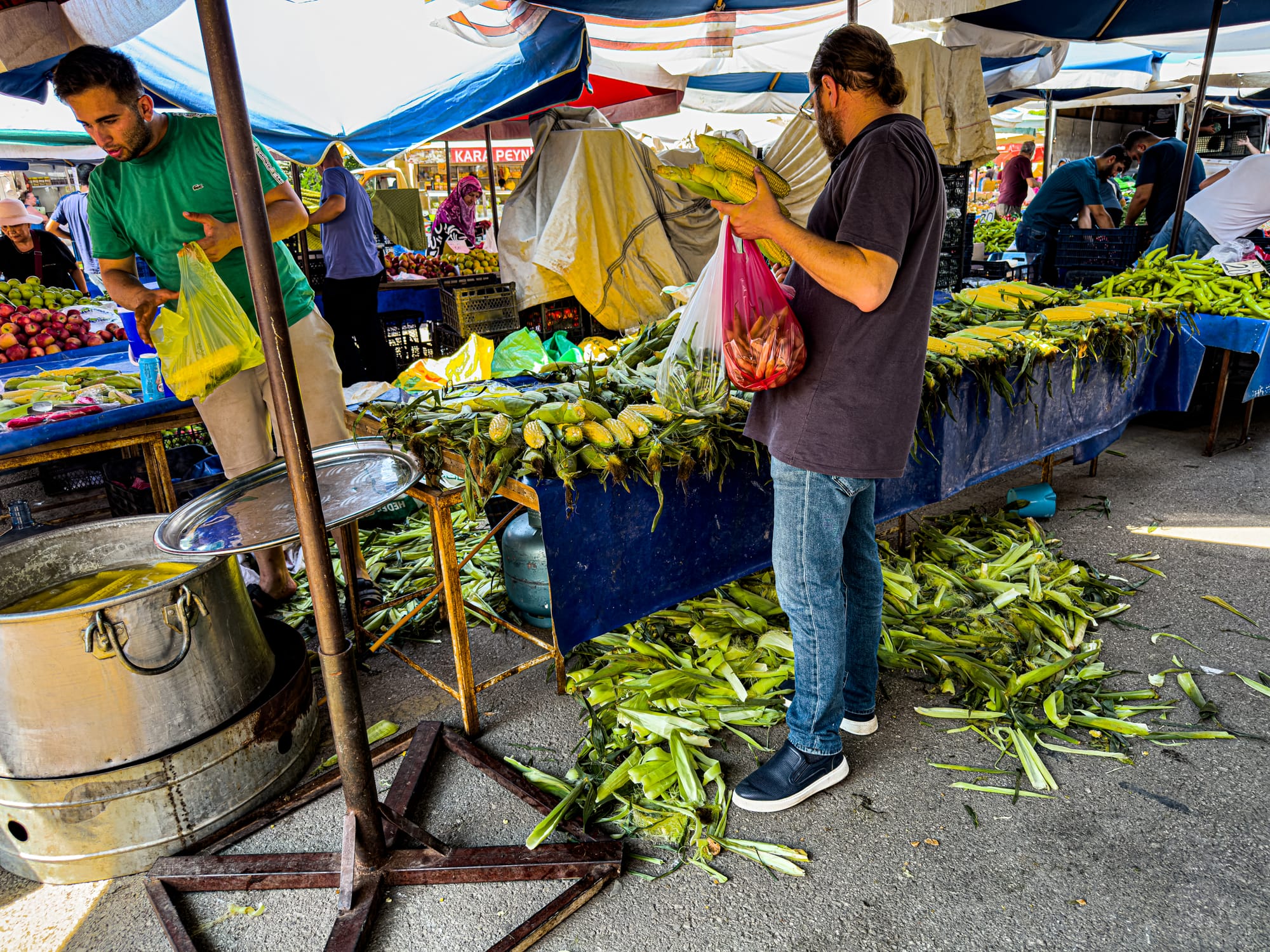 Shoppers buying corn on the cob at Antalya’s Friday Market with husks scattered across the ground