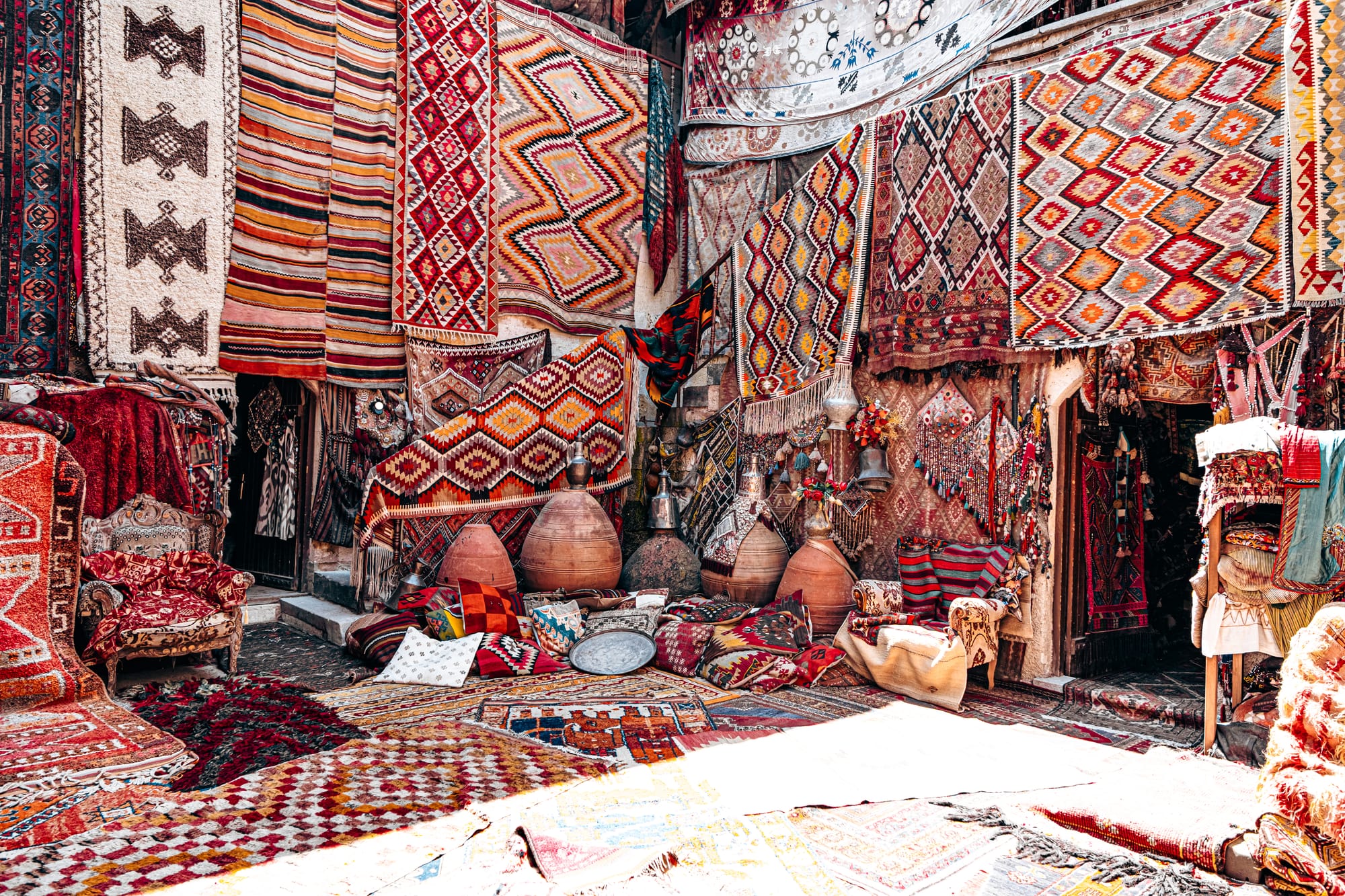 Courtyard of Galerie İkman in Göreme, overflowing with vibrant Turkish rugs hanging from walls, patterned cushions, large clay pots, and traditional decorative items