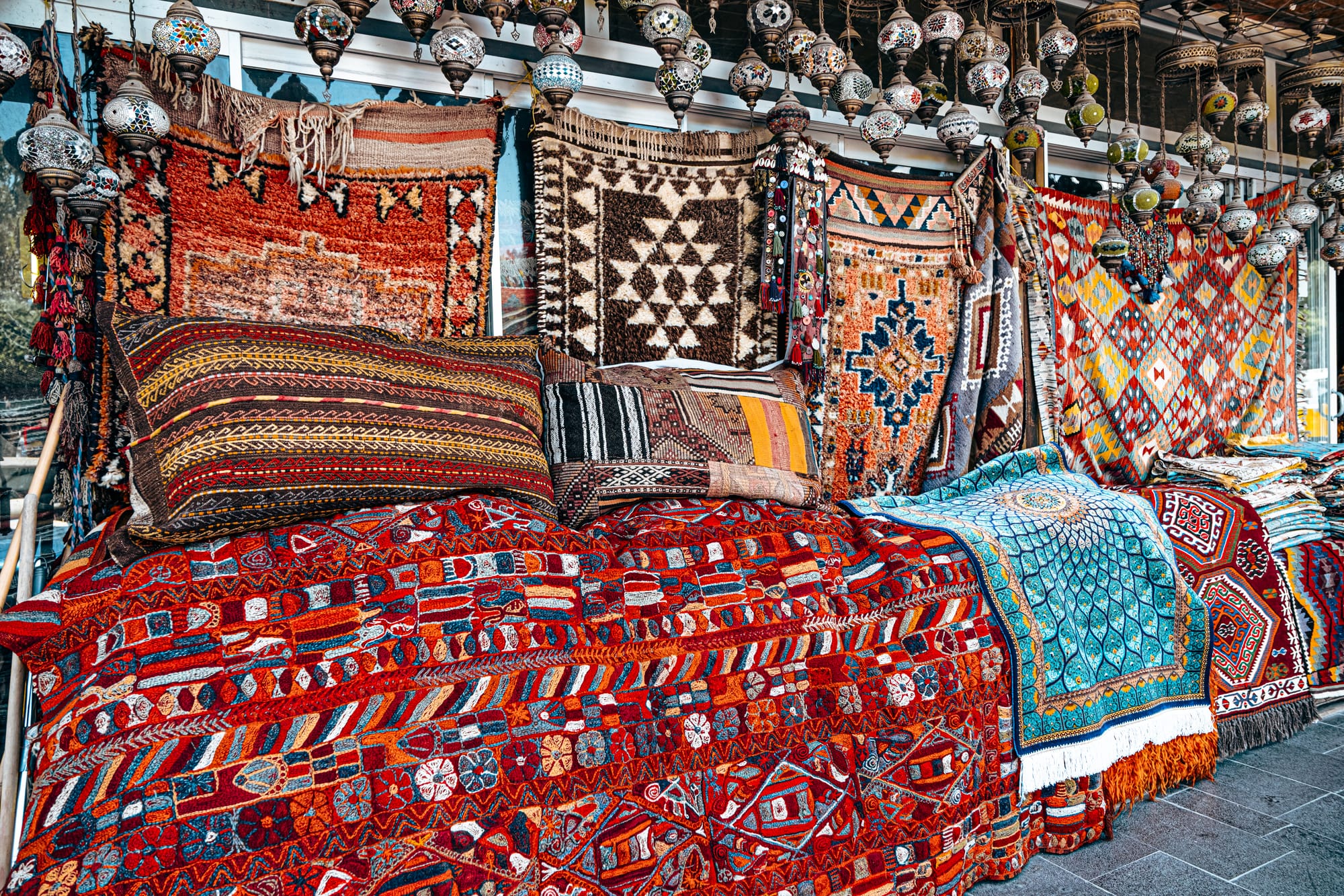 Display of vibrant handwoven Turkish carpets, kilims, and cushions in Göreme, Cappadocia, with colorful geometric patterns and hanging mosaic lamps above