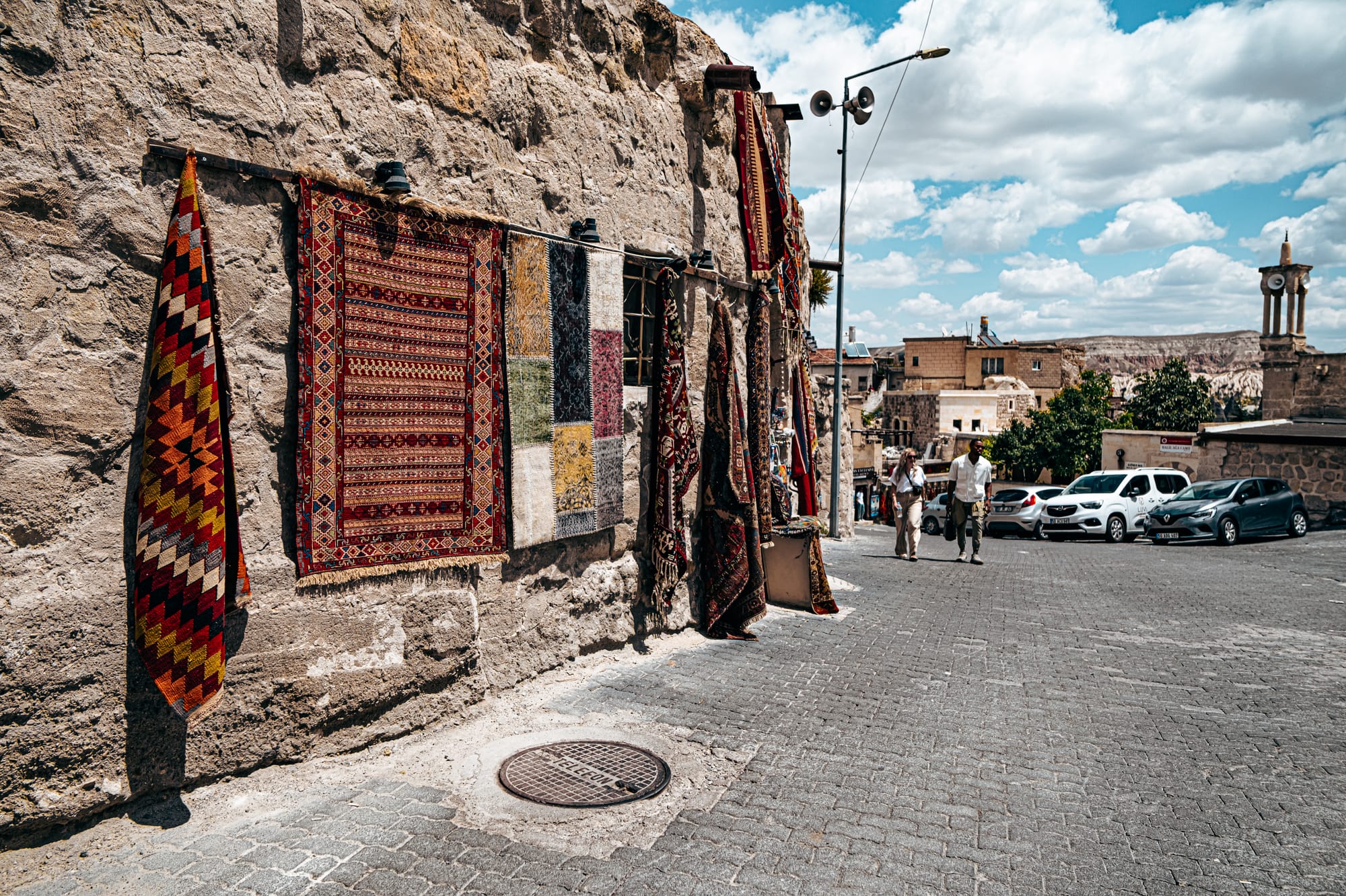 A narrow cobblestone street in Göreme lined with stone houses, carved rock facades, hanging gourds, and pottery decorations, capturing the blend of traditional architecture and artisanal details in Cappadocia’s most iconic town