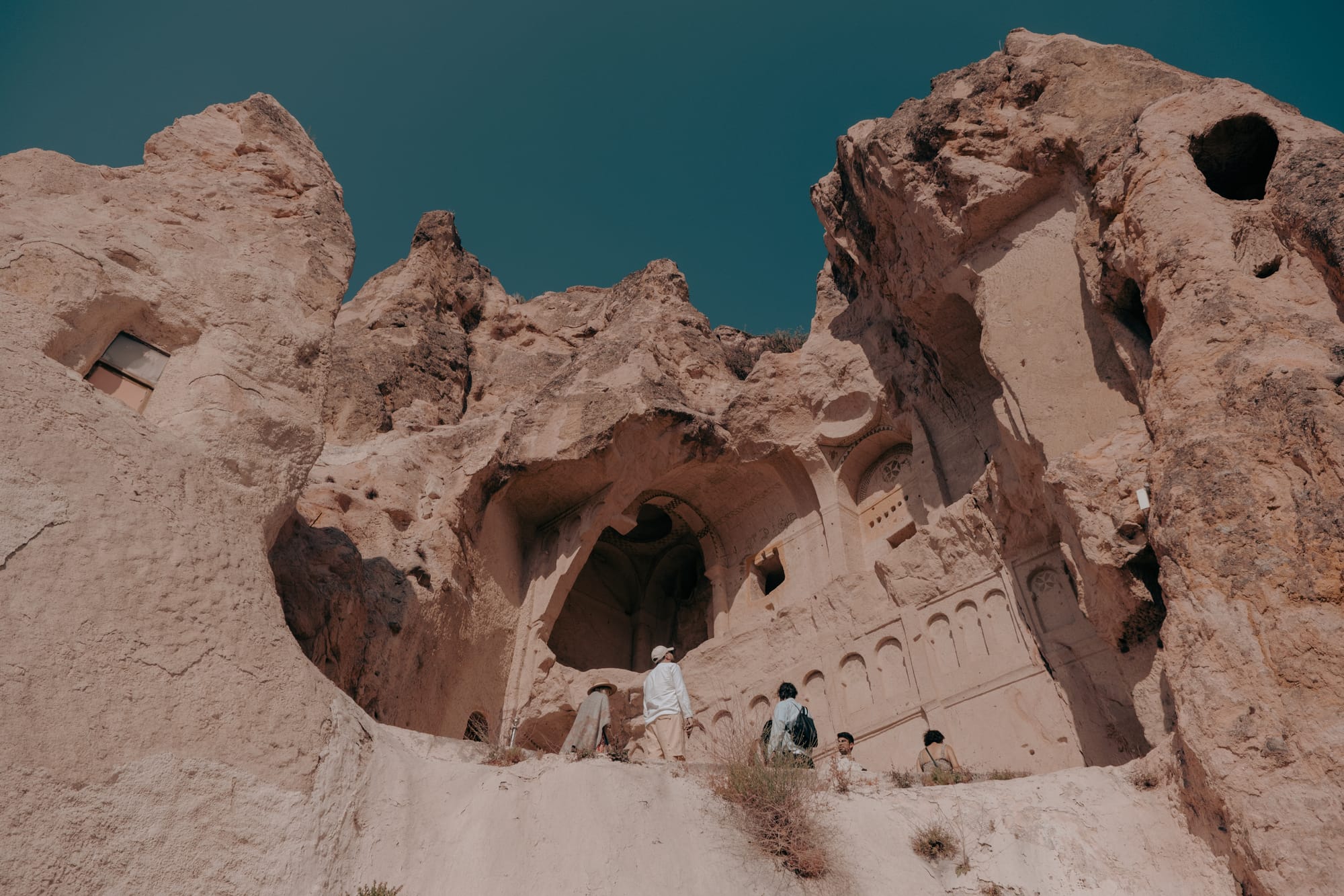 Visitors exploring a large rock-carved church facade with arches and intricate carvings at Göreme Open Air Museum in Cappadocia