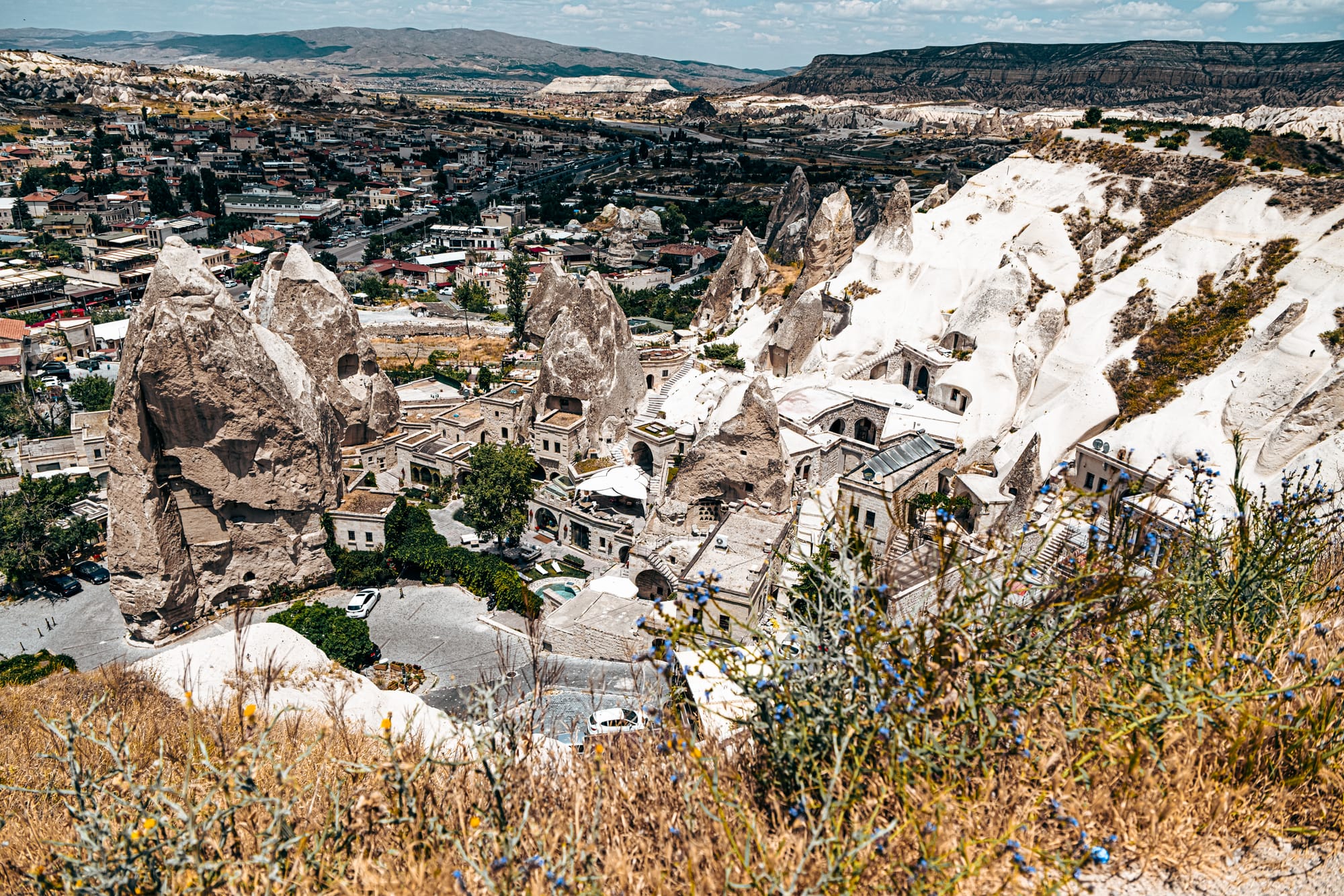 Elevated view of Göreme town showing tall rock pinnacles, cave houses, and white volcanic slopes surrounded by modern buildings and roads