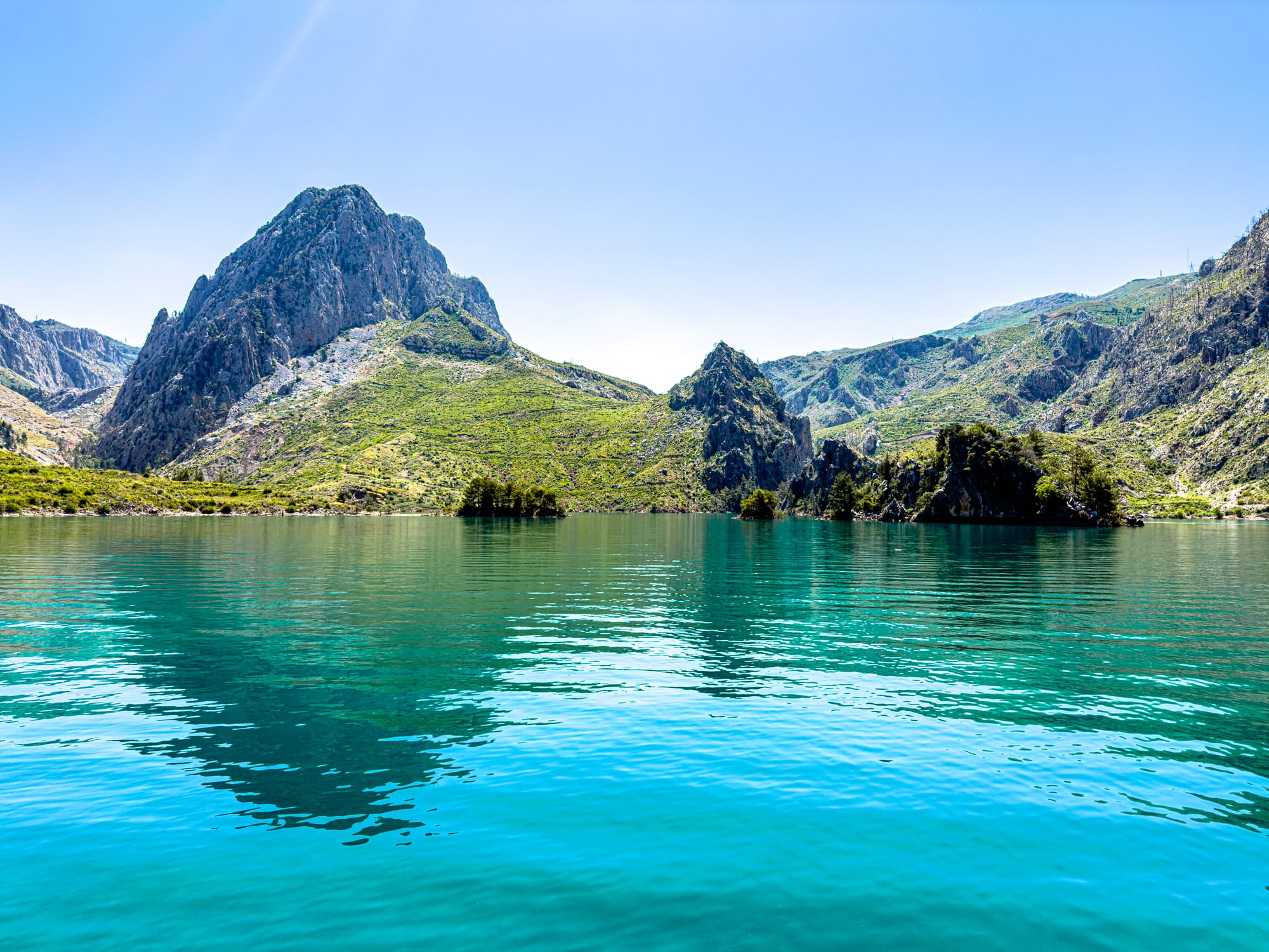 A tranquil view of Green Canyon with turquoise water reflecting rugged green mountains under a clear blue sky