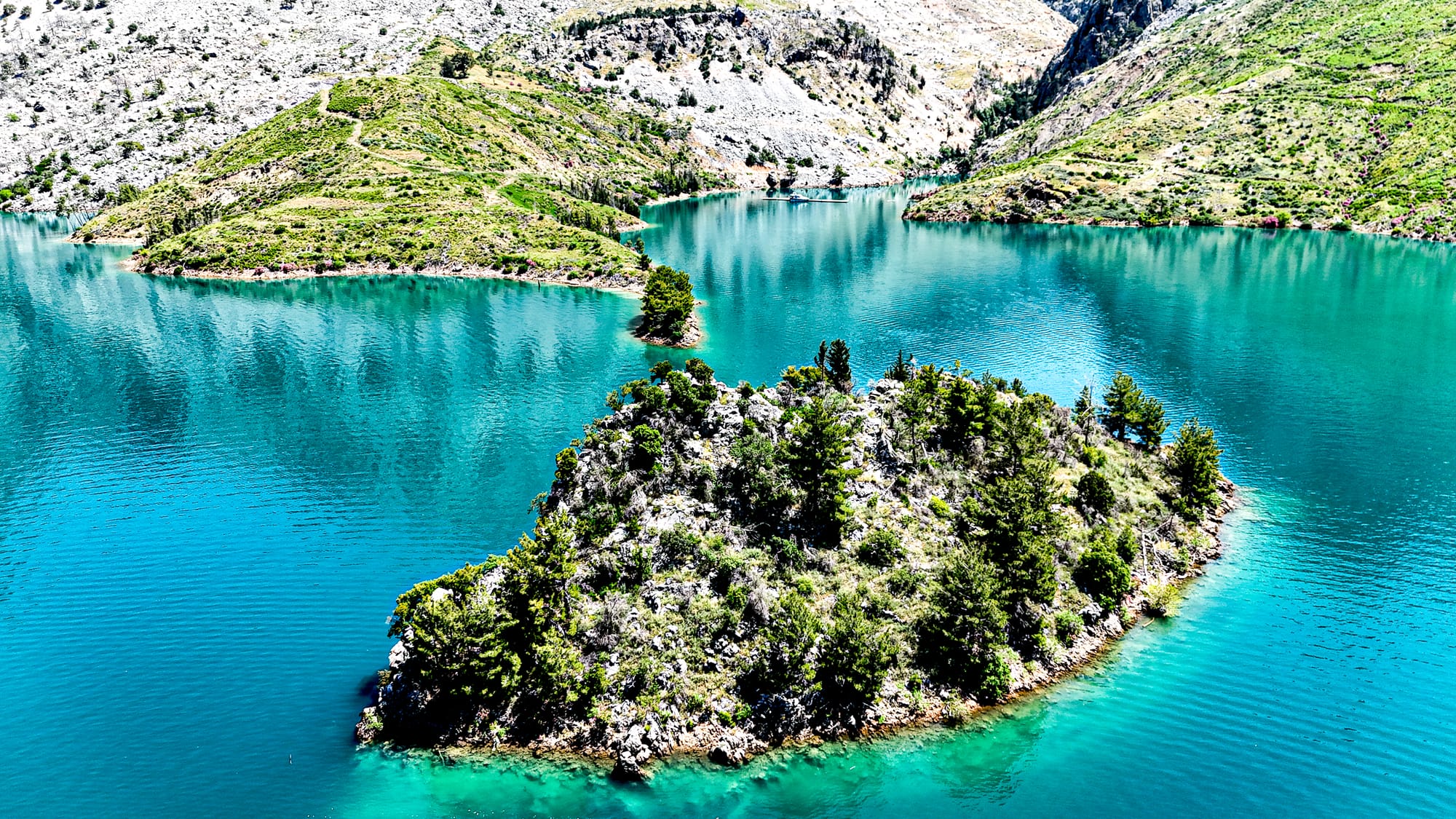 Small forested islets scattered across Green Canyon’s turquoise reservoir, framed by steep mountain slopes and rocky terrain