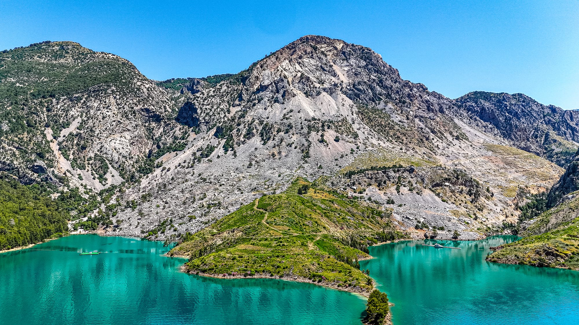 View of a jagged mountain ridge rising above turquoise waters and a green peninsula in Turkey’s Green Canyon