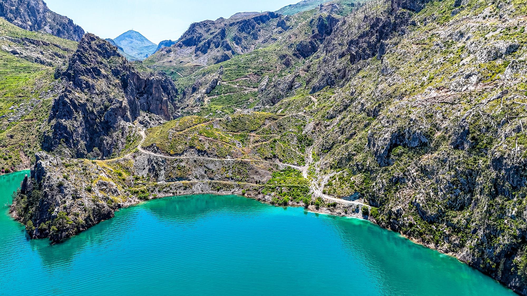 Aerial view of the Green Canyon in Turkey showing turquoise lake water surrounded by rocky mountains with zigzagging dirt trails