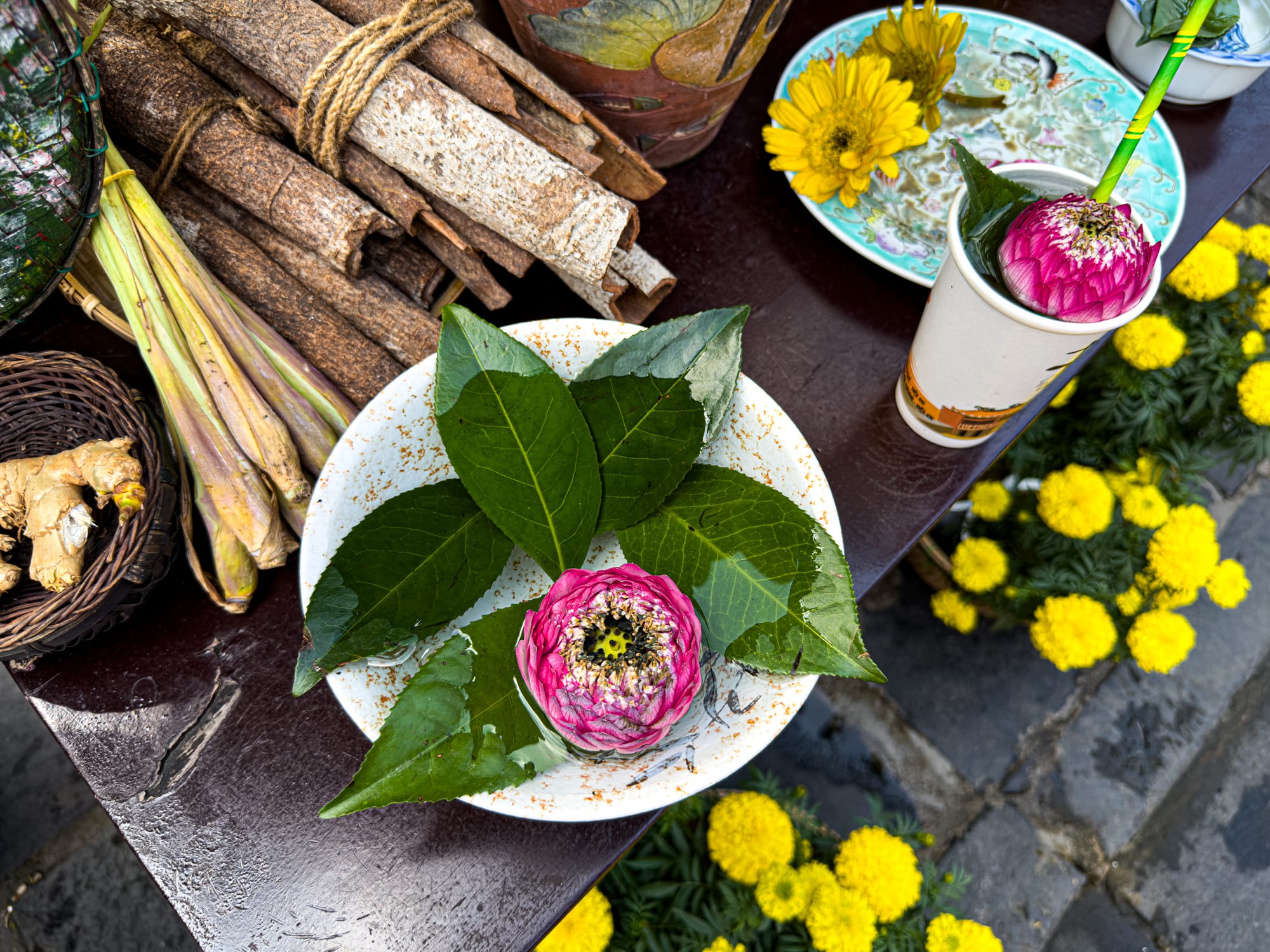 Close-up of herbal tea ingredients, fresh ginger, cinnamon, and lotus flowers arranged on a street stall in Hội An’s Old Town, Vietnam, reflecting local culture and tradition