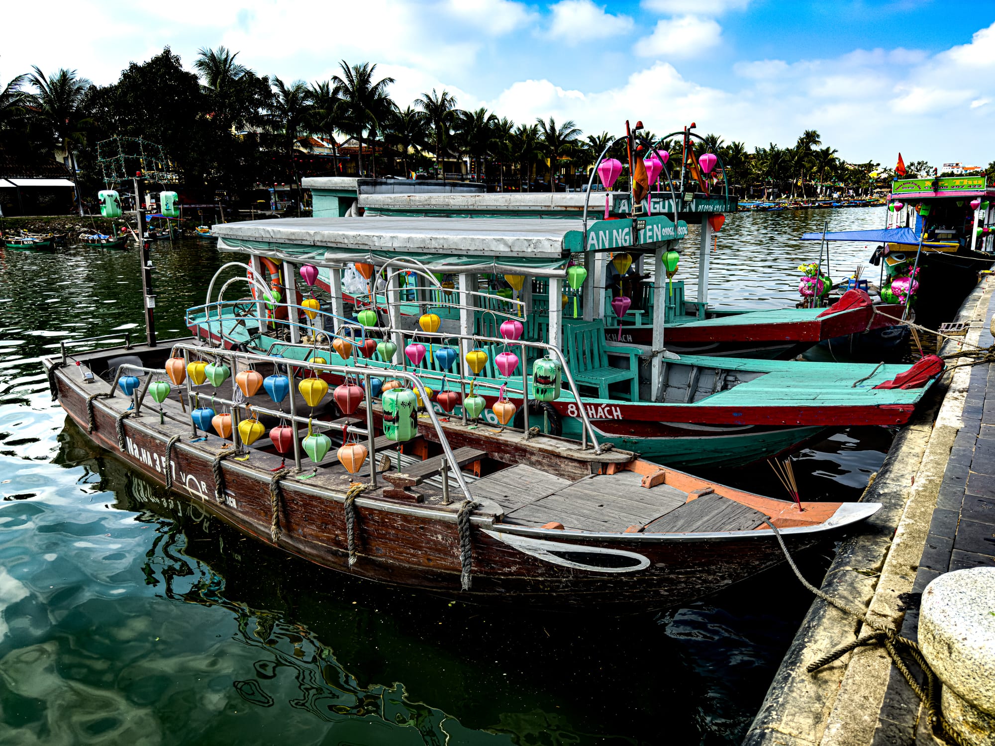 Traditional wooden boats decorated with colorful silk lanterns docked along the river in Hội An’s Old Town, Vietnam, offering lantern boat rides at night