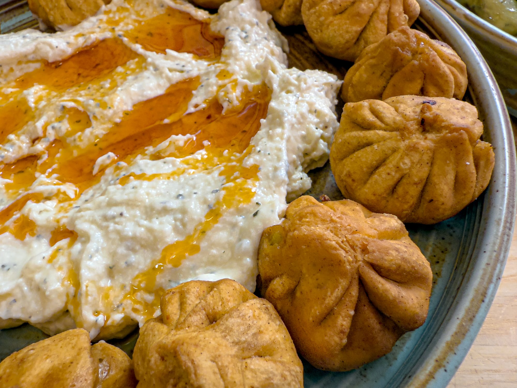 Close-up of golden vegan momos surrounding a swirl of housemade yogurt topped with chili oil