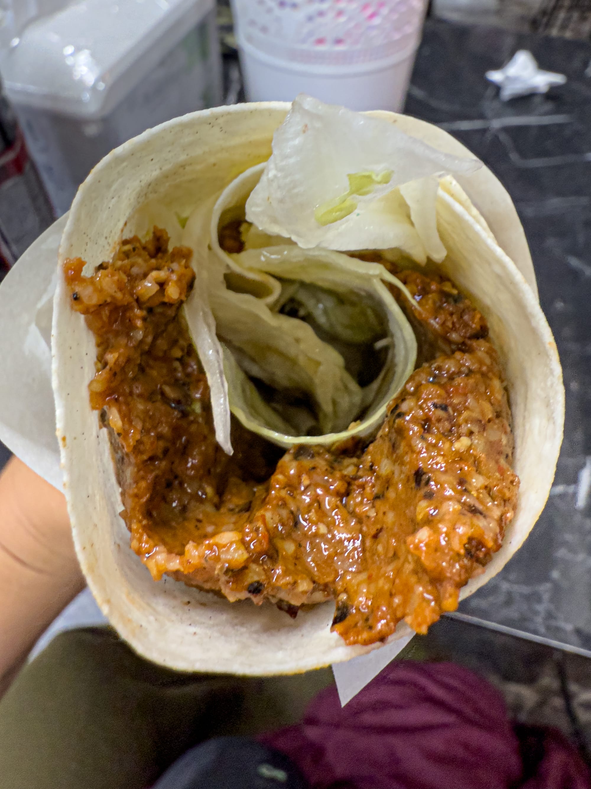Close-up of a hand holding a Turkish çiğ köfte wrap filled with spiced bulgur and lettuce