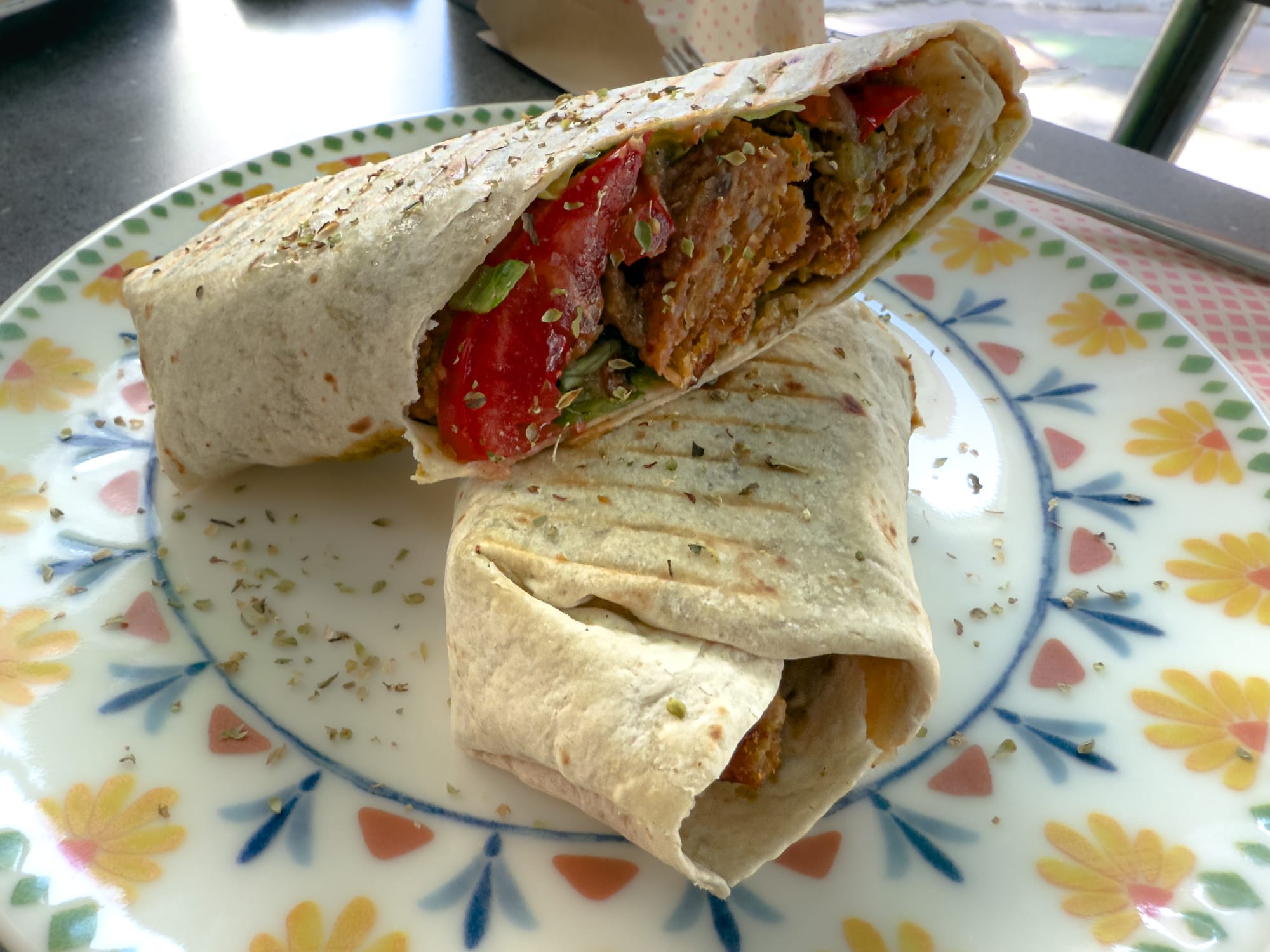 Close-up of a vegan wrap from Veganarsist Kadıköy, filled with lentils, tomatoes, and greens, served on a floral-patterned plate