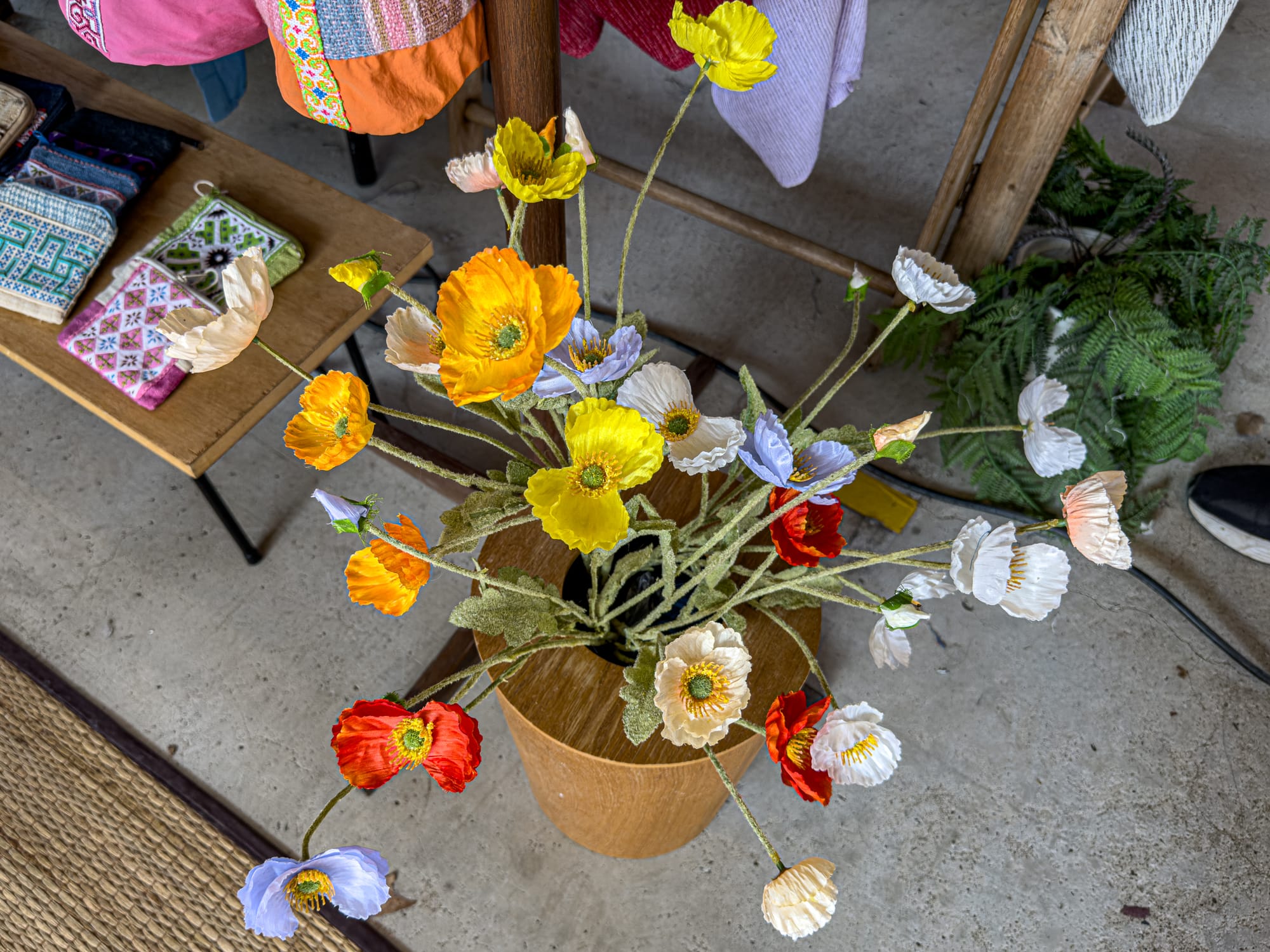 A vibrant bouquet of handmade paper flowers in shades of yellow, orange, red, white, and purple, displayed in a wooden vase at Jing Jai Market in Chiang Mai