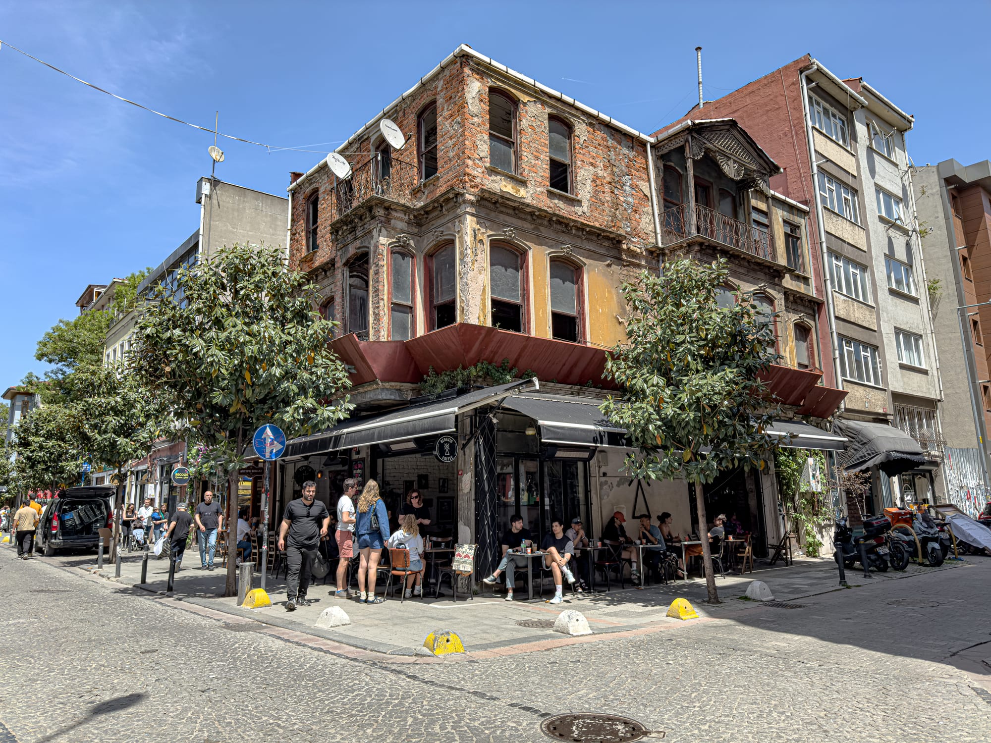 A lively street corner in Kadıköy, Istanbul, where people sit at an outdoor café beneath a weathered, partially crumbling historic building
