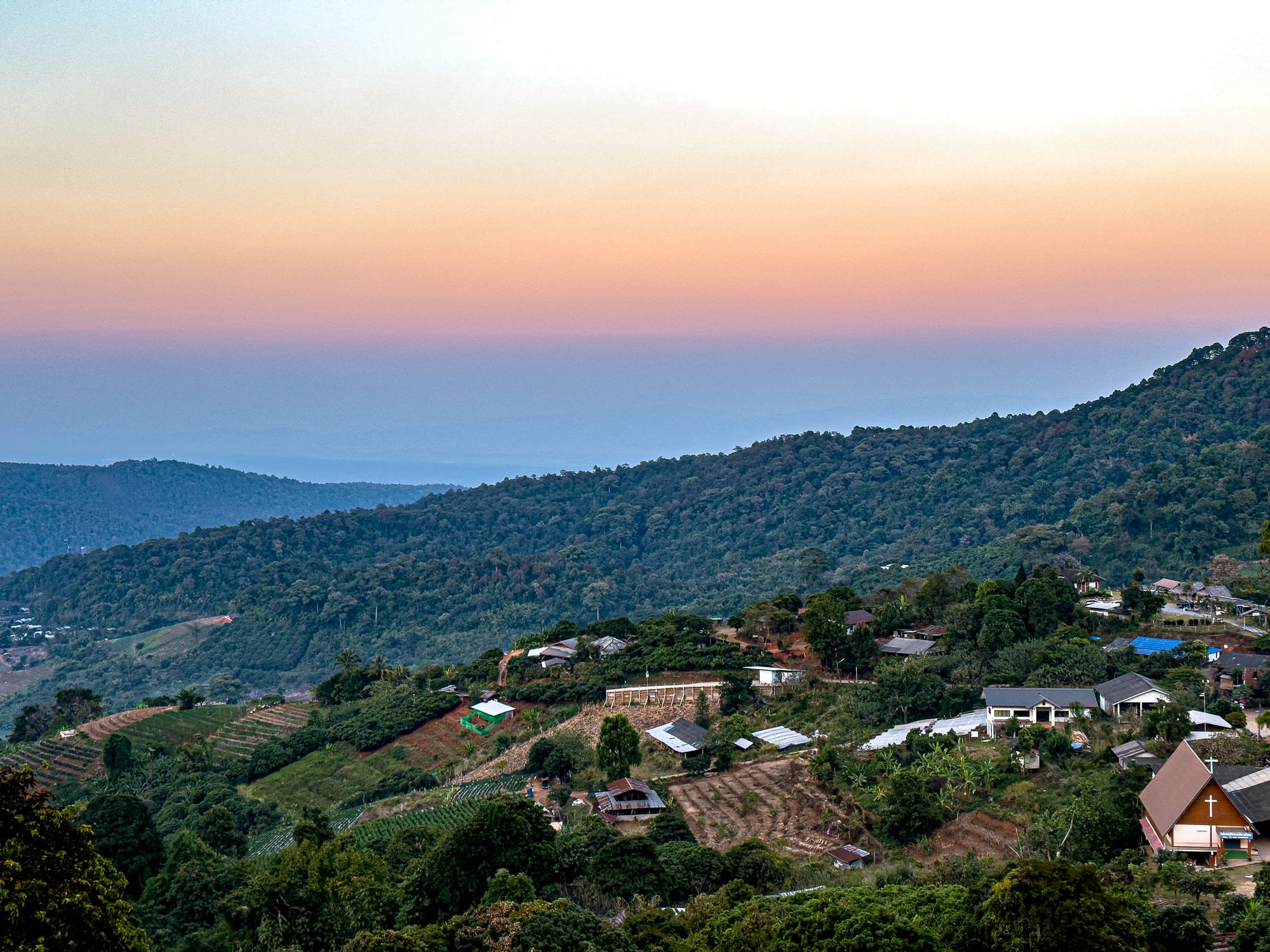Panoramic view of Mae Rim hills at sunset, with colorful sky gradients and scattered houses among green forested slopes
