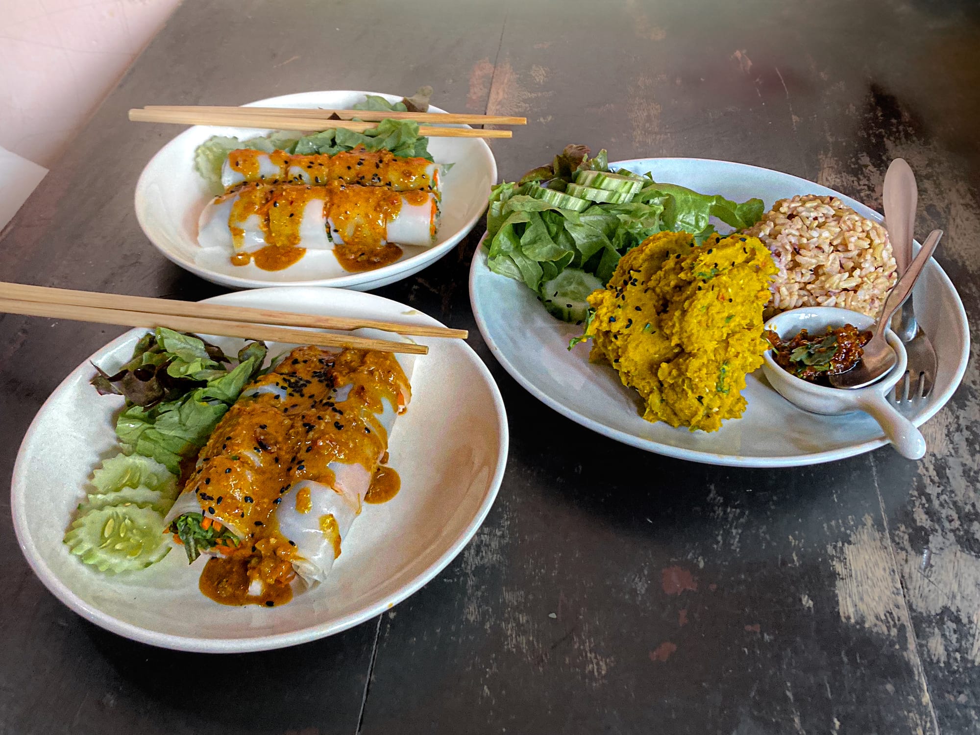 A table setting at May Kaidee restaurant featuring two plates of fresh spring rolls with peanut sauce and a large plate with leafy greens, rice, and the restaurant’s famous bright orange pumpkin hummus