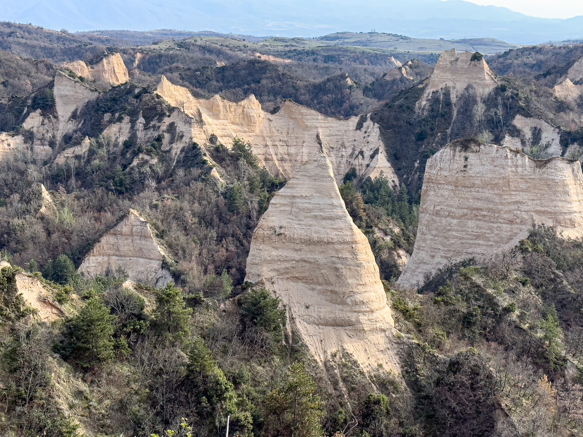 View of the Melnik Earth Pyramids in Bulgaria, with steep sandstone spires and ridges rising above forested valleys