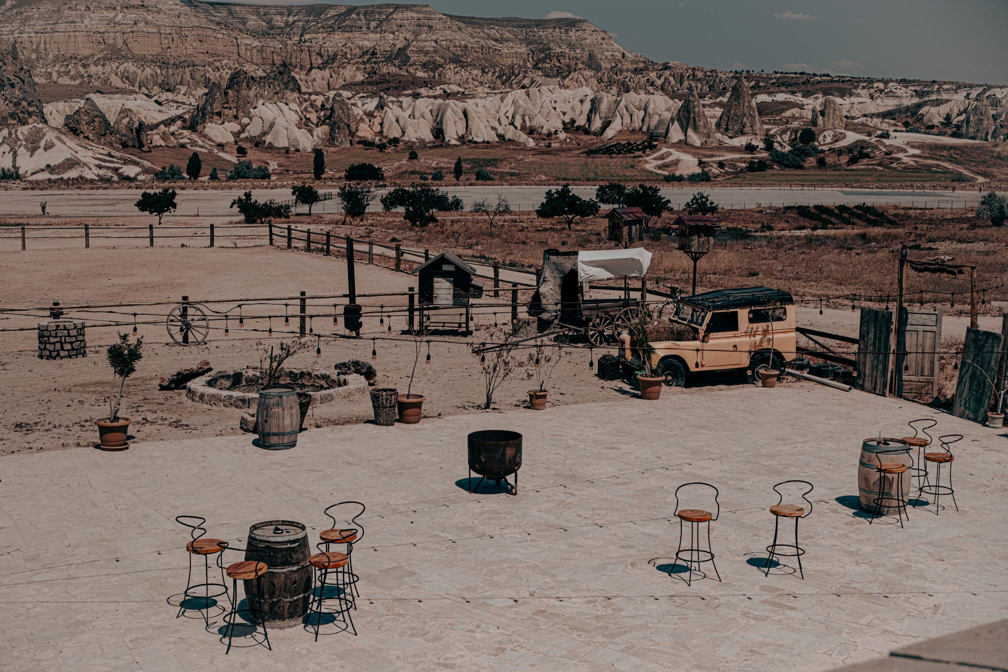 Courtyard at Moonlight Ranch in Cappadocia, featuring rustic barrel tables, chairs, vintage wagon, and mountain backdrop