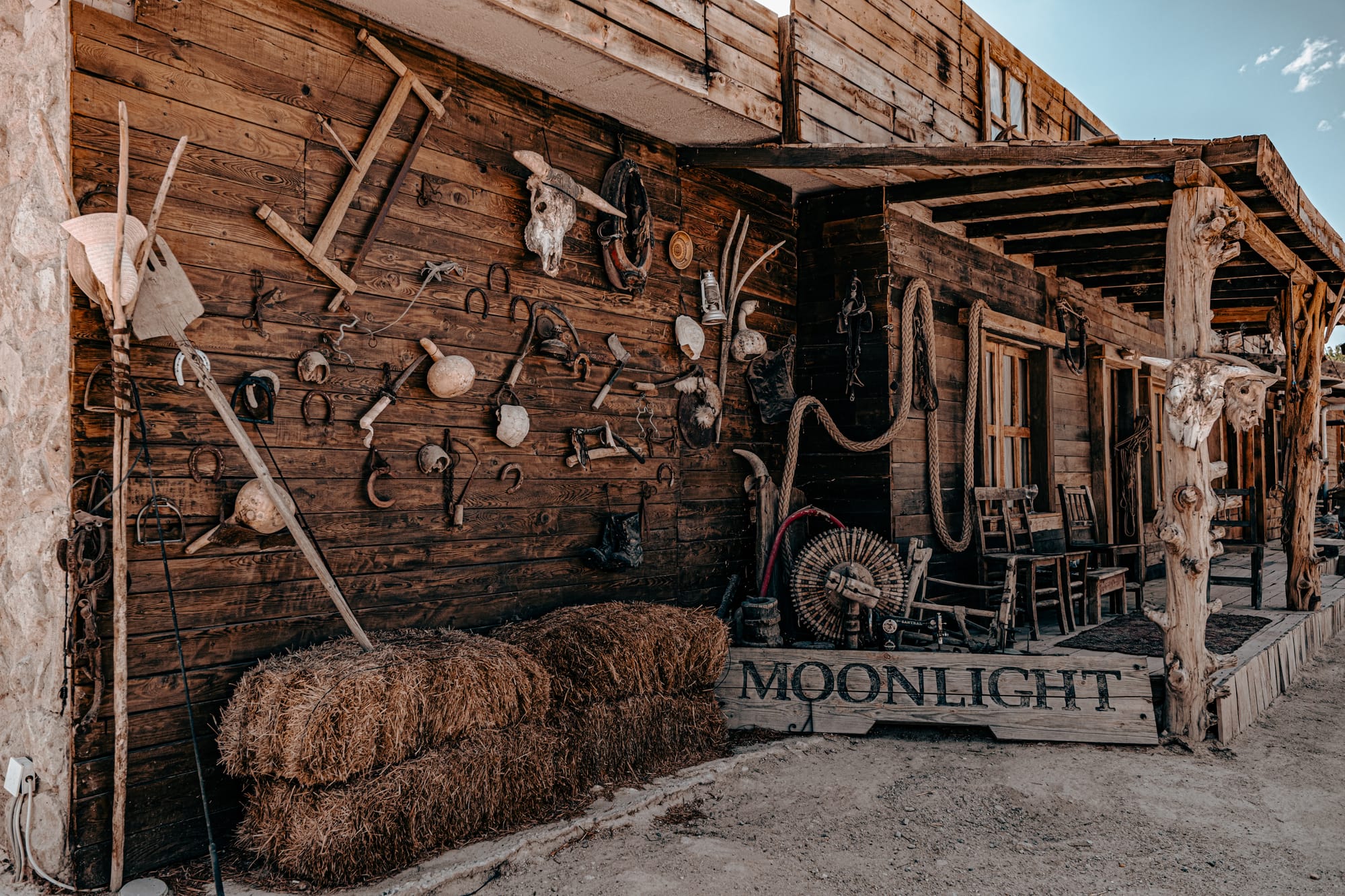 Rustic wooden facade at Moonlight Ranch in Cappadocia, decorated with vintage farm tools, horse tack, ropes, and a mounted cow skull, alongside hay bales and a weathered “Moonlight” sign, evoking an Old West frontier town aesthetic