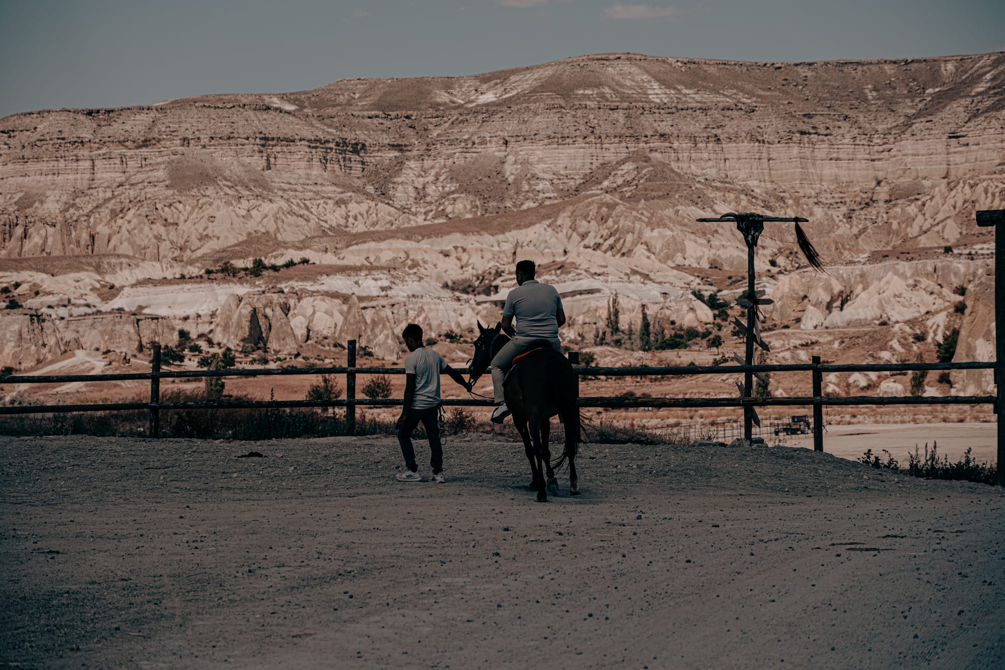 A guide leading a saddled horse carrying a rider at Moonlight Ranch in Cappadocia, Turkey, with striking mountain formations and rugged cliffs visible in the background