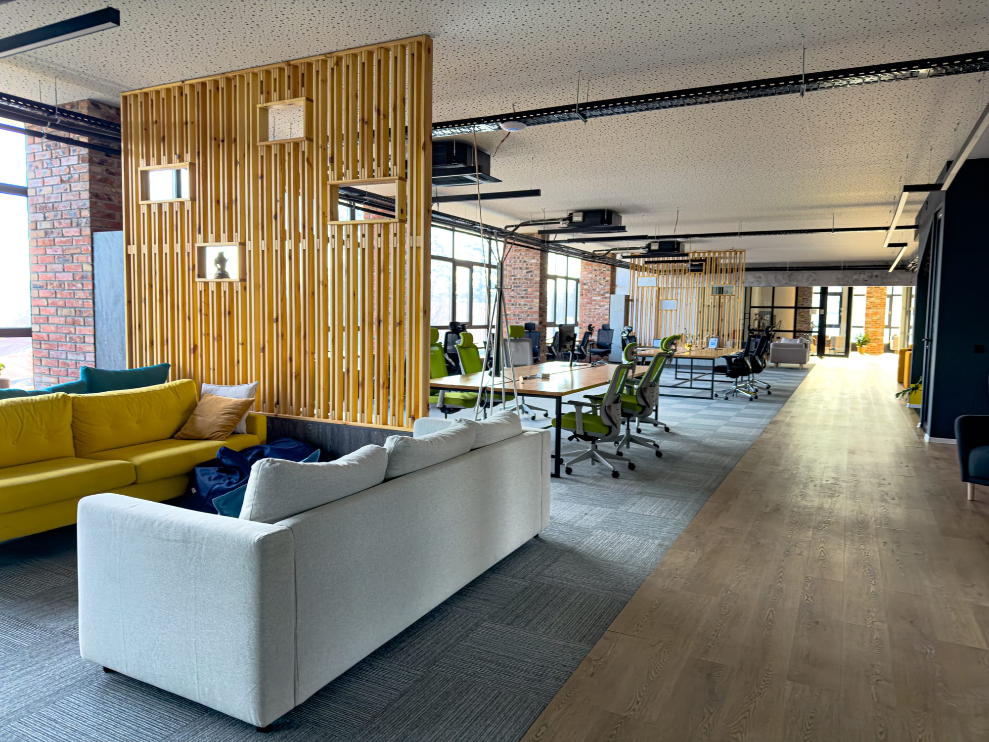Interior of Nestwork coworking space in Bansko, showing an open-plan layout with modern green office chairs, long wooden desks, and bright sofas separated by wooden partitions, creating a spacious and contemporary work environment