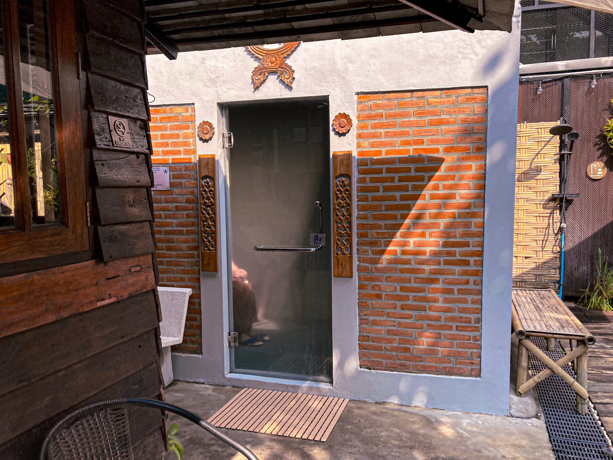 Exterior of the herbal steam room at Old City Spa in Chiang Mai, with brick walls, wooden carvings, and a glass door leading inside