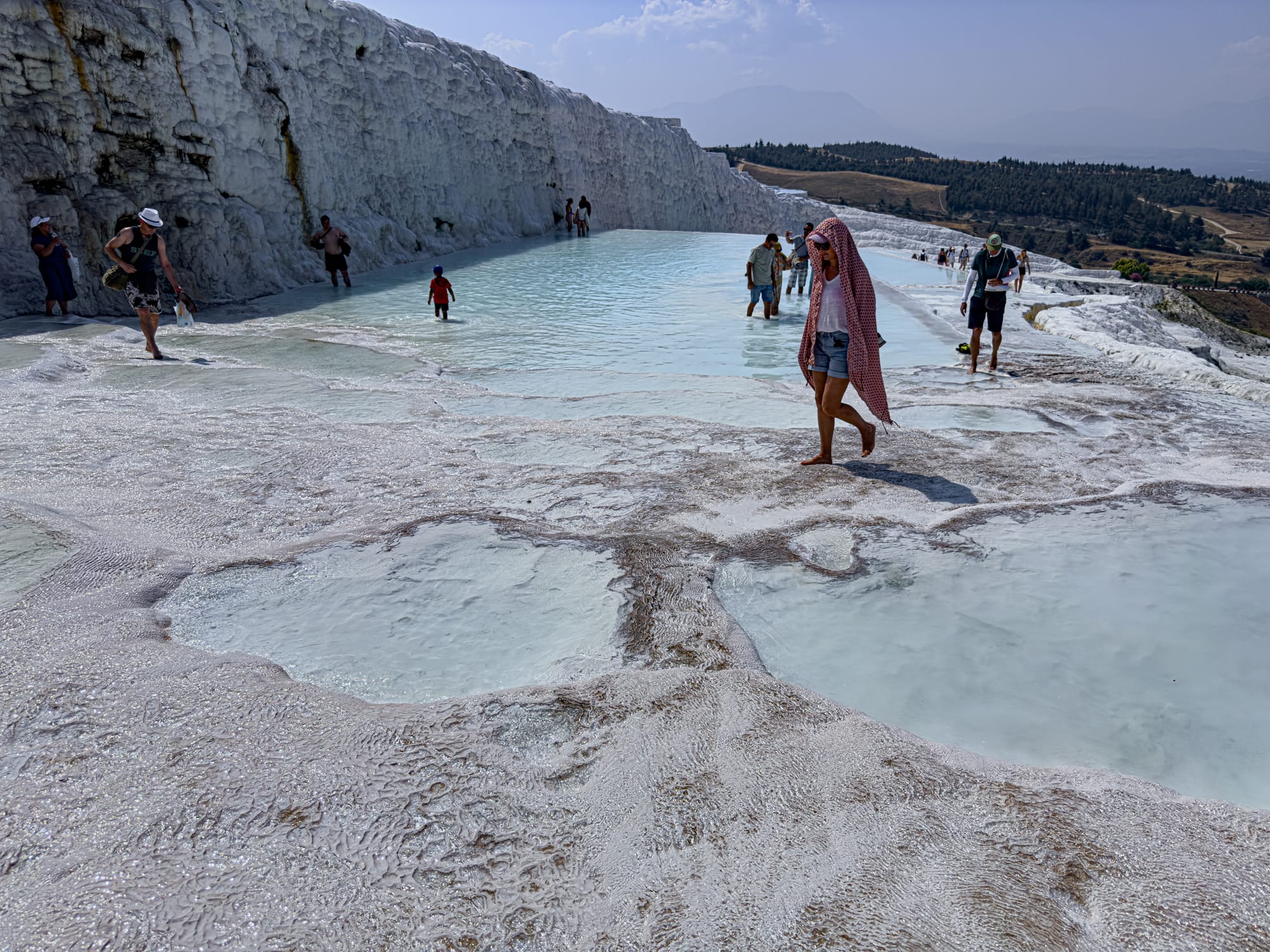 Visitors walking barefoot across the textured white calcium terraces and shallow pools of Pamukkale