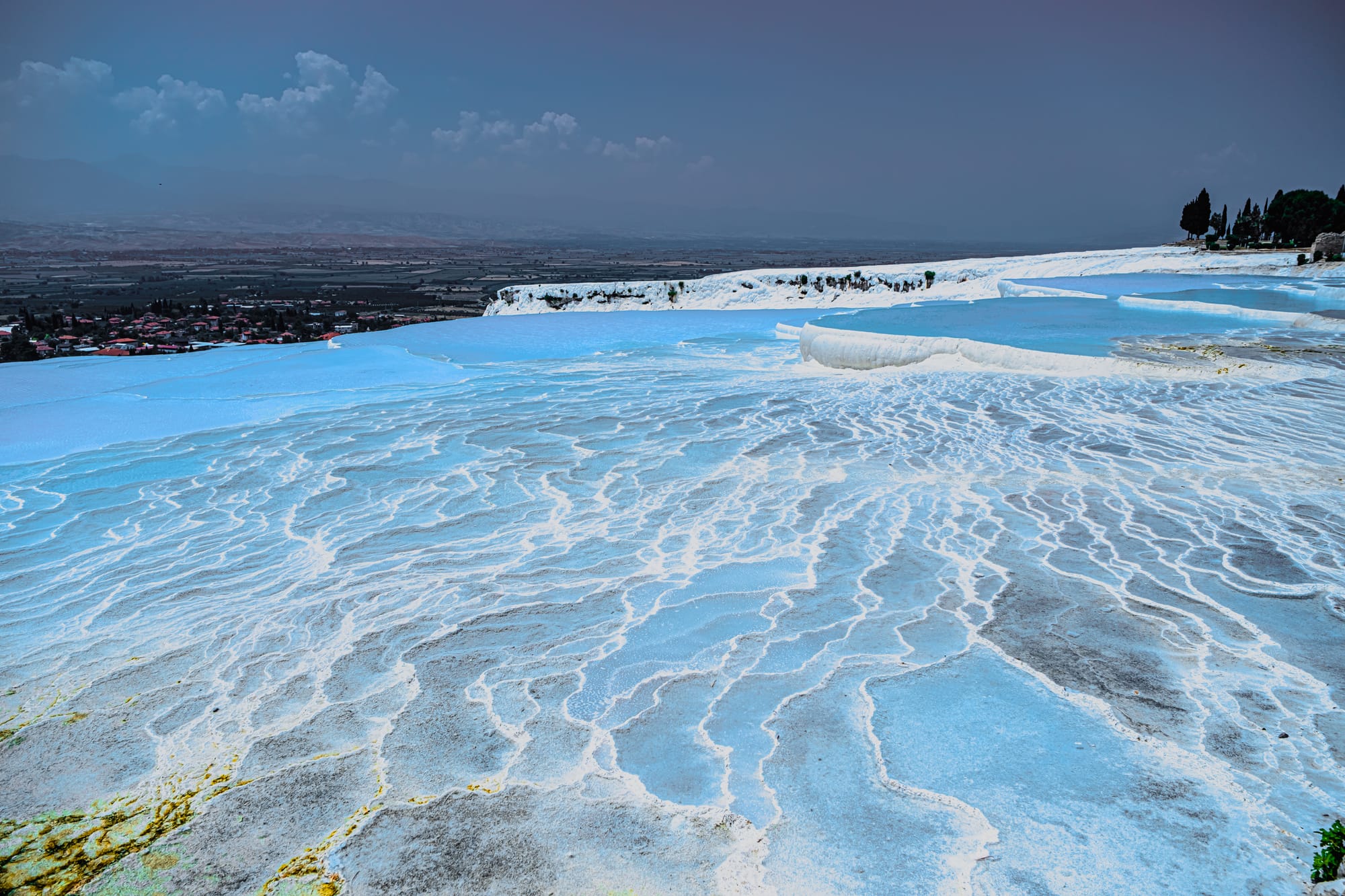 Pamukkale’s travertine terraces shimmering in layered blues and whites, stretching toward the distant valley