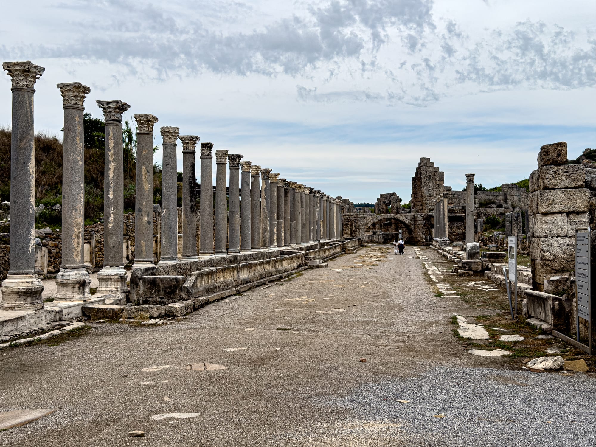 Colonnaded main street of Perge with long rows of Roman columns and stone ruins under a cloudy sky near Antalya, Turkey