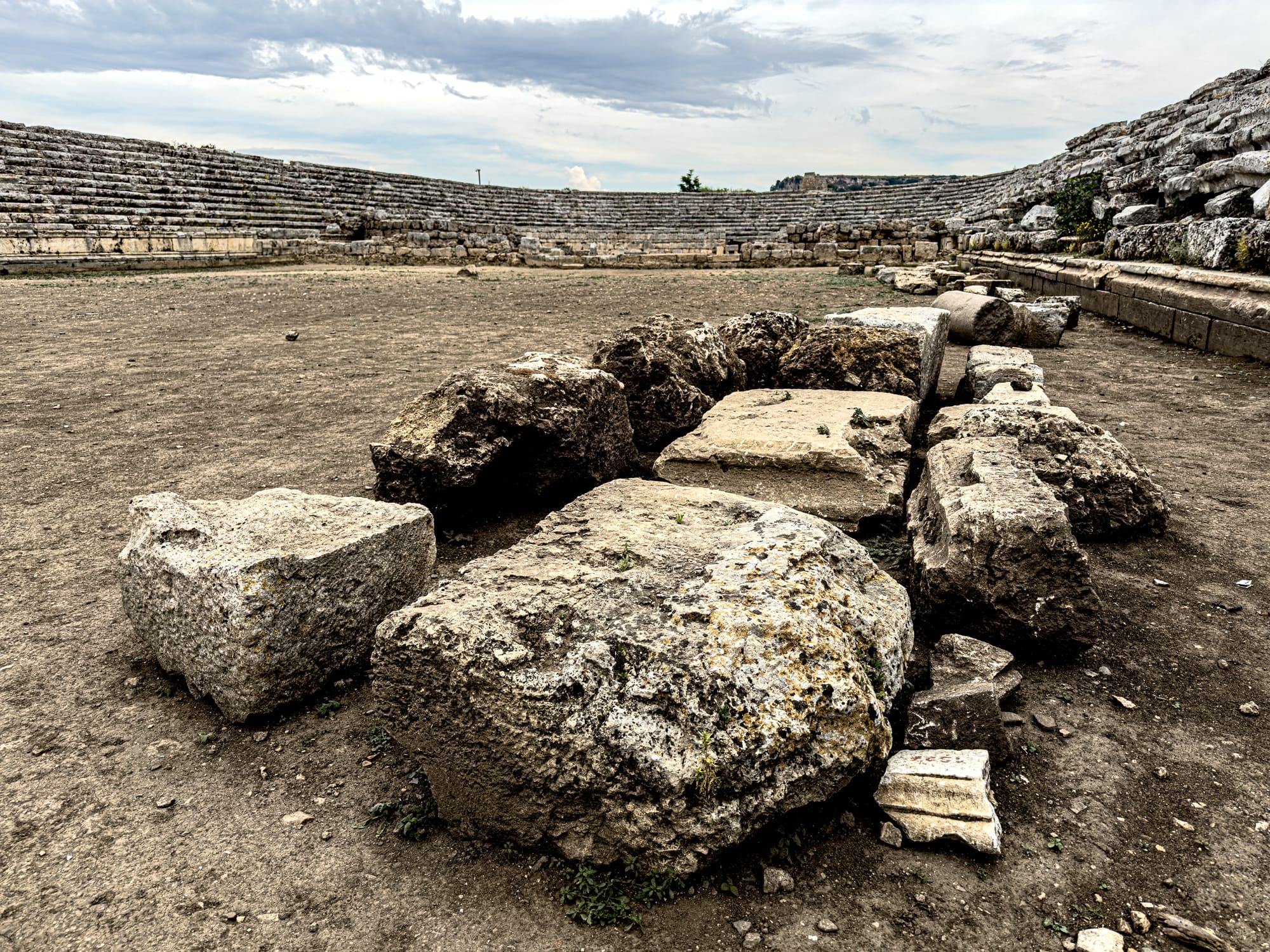 Stone blocks scattered on the ground inside the Roman stadium at Perge with curved spectator seating in the background near Antalya, Turkey