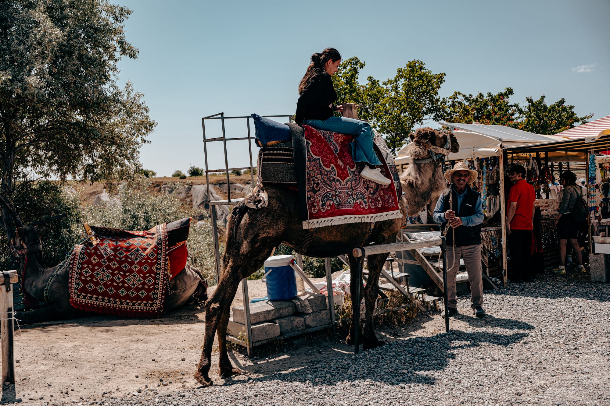Tourist sitting on a saddled camel at Pigeon Valley Lookout in Cappadocia with vendor nearby
