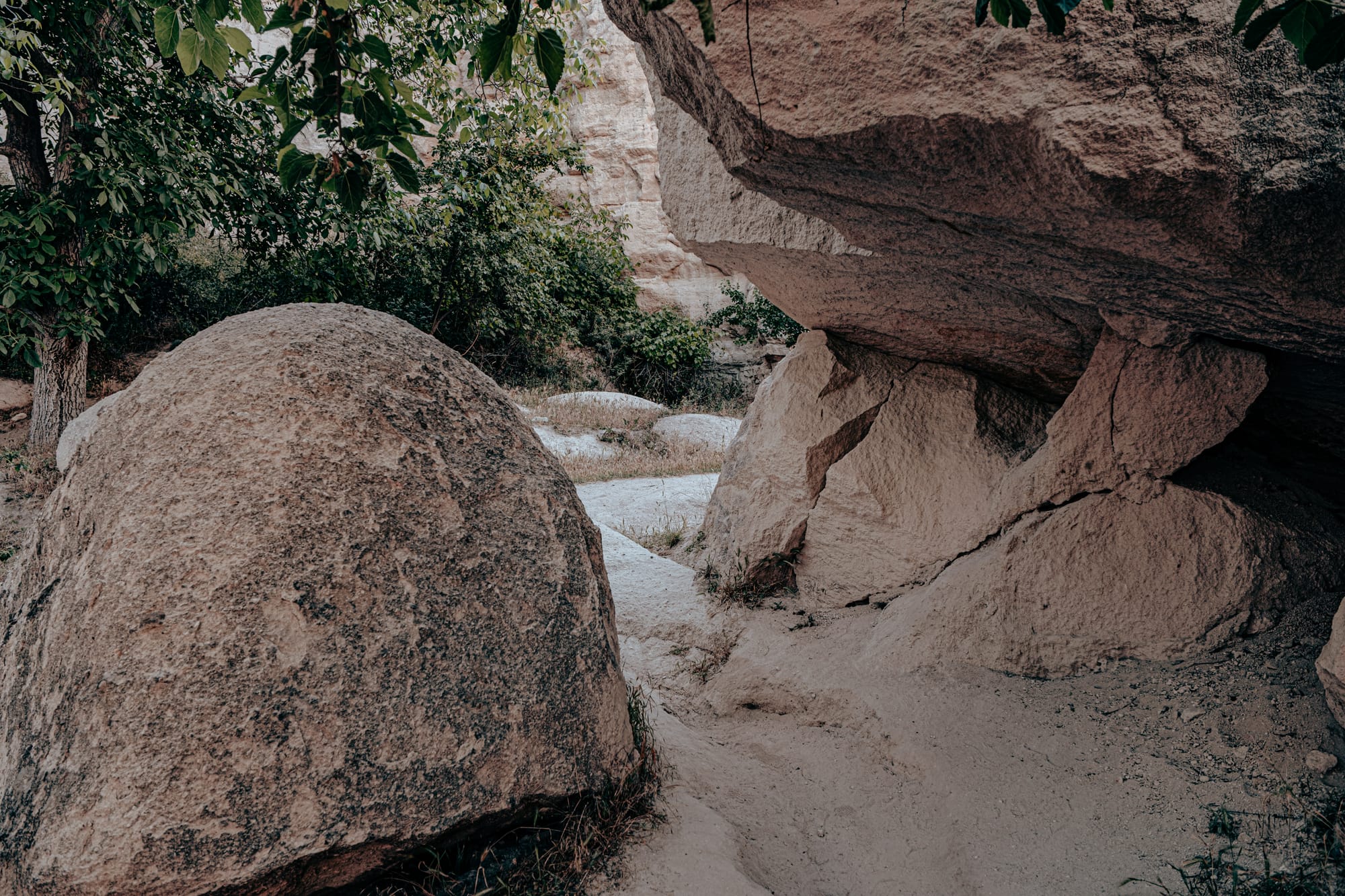 Two large weathered boulders in Pigeon Valley, one upright and one overhanging, creating a shaded rocky passage with glimpses of white sand and greenery beyond