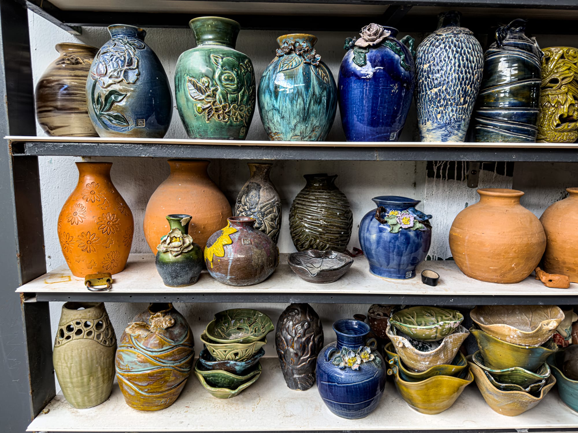 Handcrafted ceramic vases and bowls displayed on shelves at Thanh Hà Pottery Village in Hội An, showcasing traditional Vietnamese pottery designs