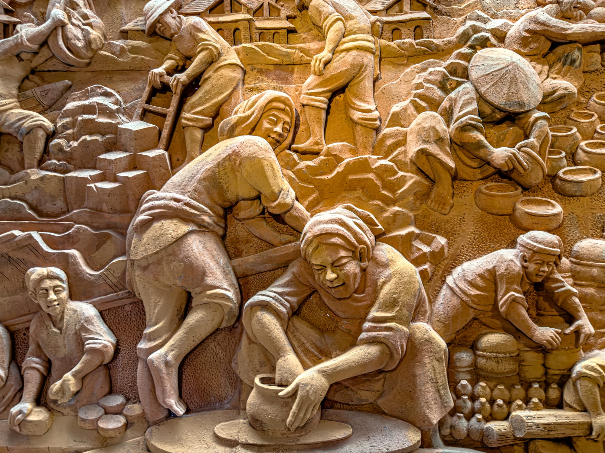 Clay bas-relief mural of artisans making and shaping pottery at the Terracotta Park in Thanh Hà Pottery Village Hội An, illustrating traditional Vietnamese ceramic craft